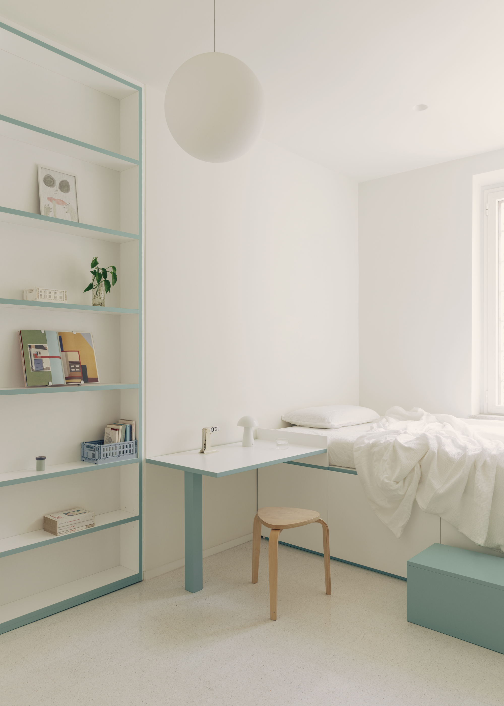 Bedroom with pale blue steel shelving unit, simple desk and spherical pendant light overhead