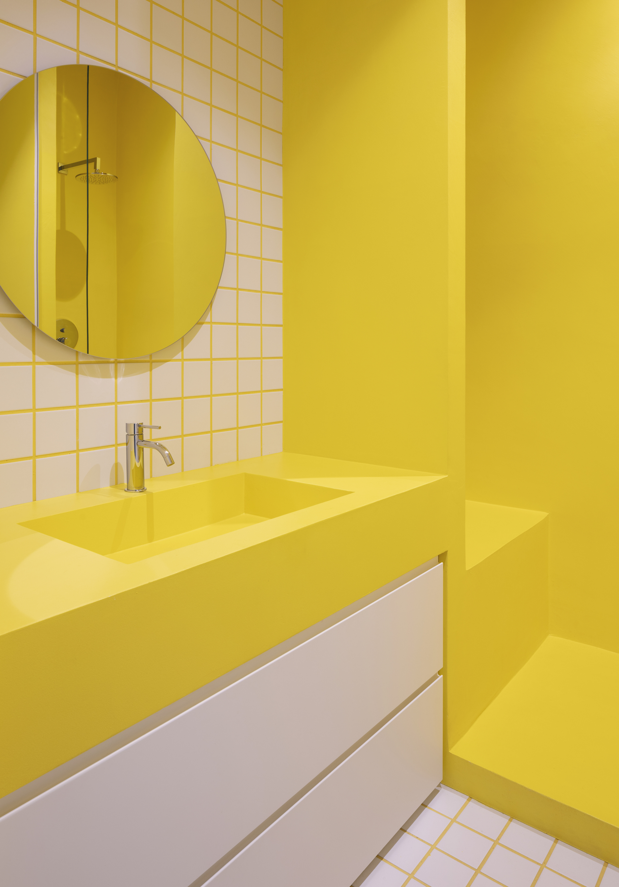 Yellow bathroom vanity with white tile wall, round mirror and chrome faucet