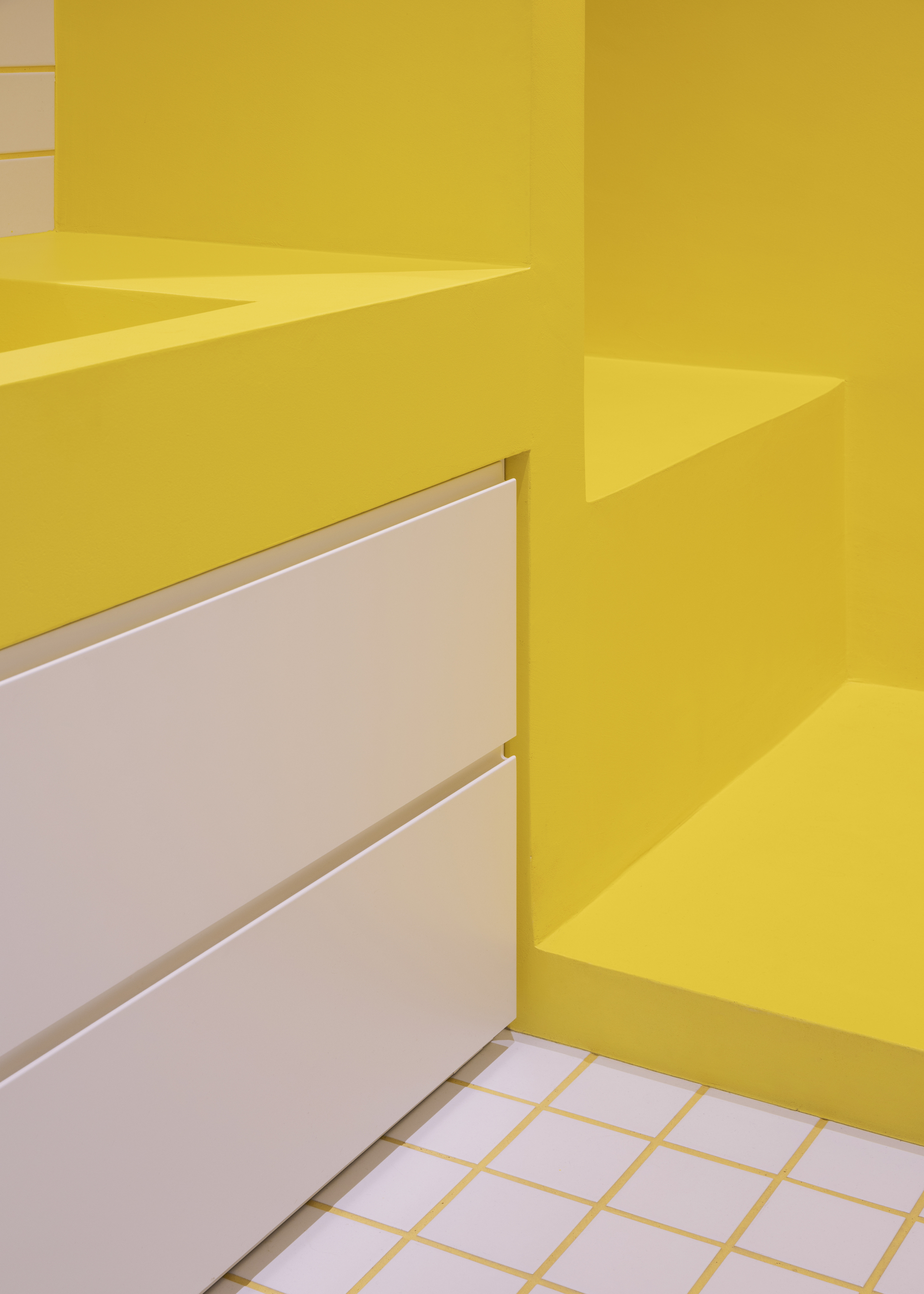 Detail of yellow countertop edge meeting white drawer fronts and grid tile floor
