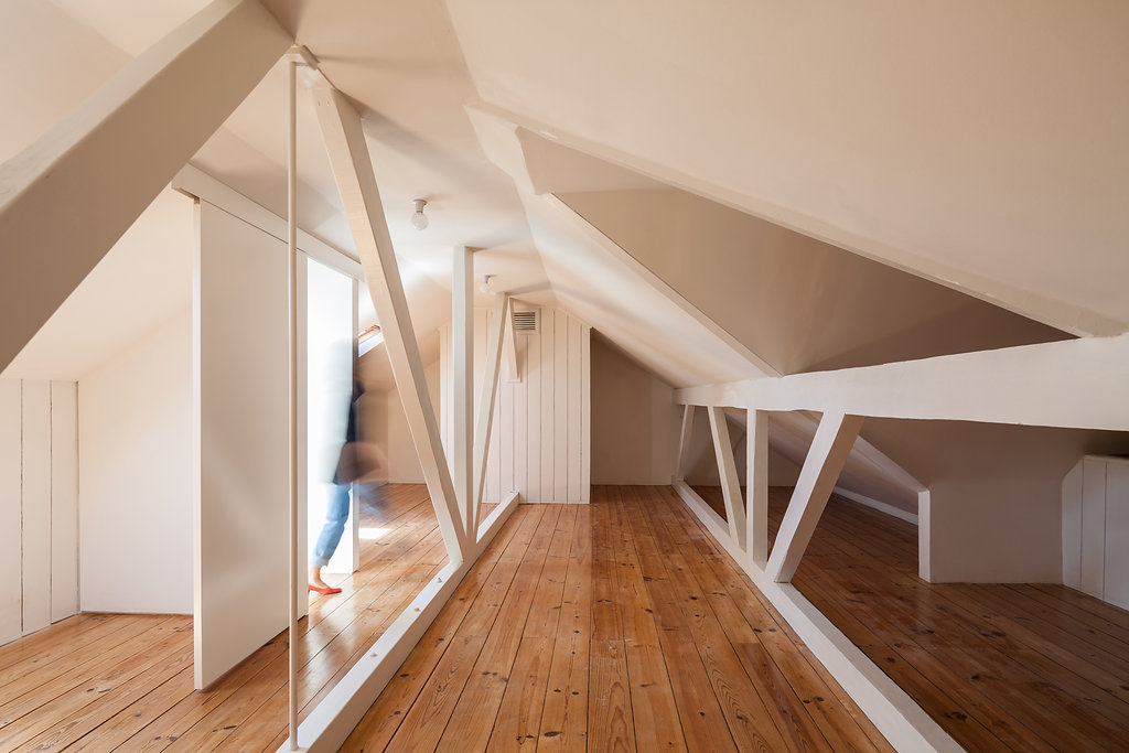 Attic room with white timber trusses, pine floorboards and sloping ceilings, a blurred figure walking past a sliding panel in soft daylight
