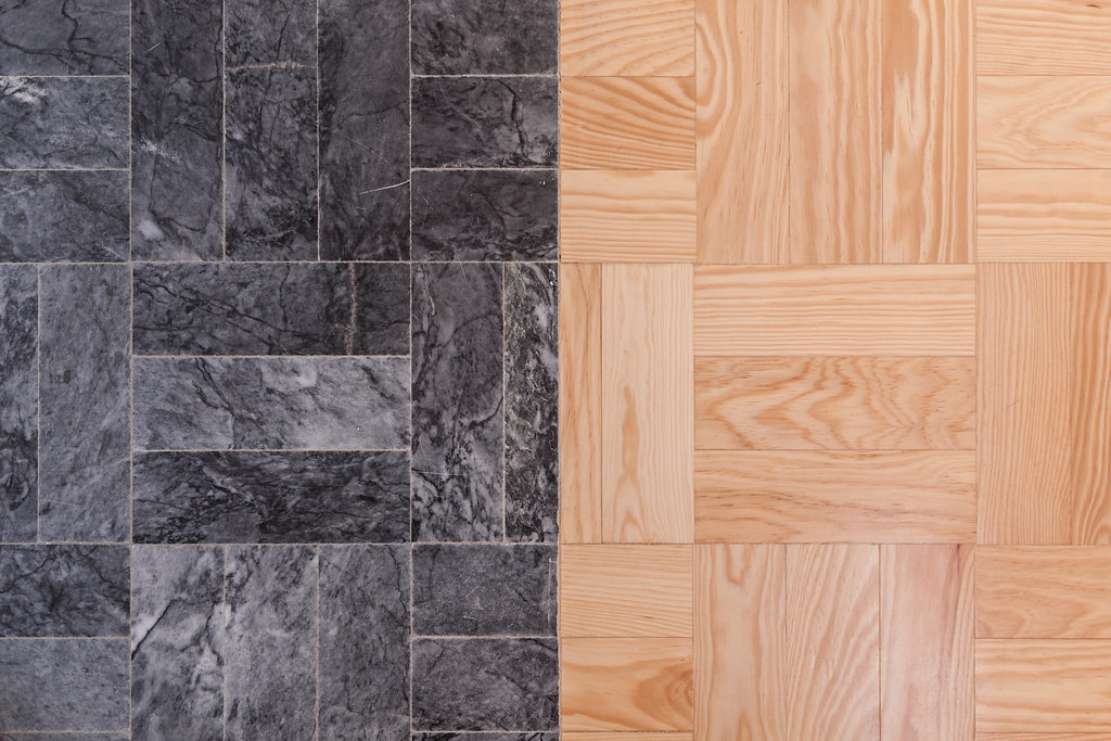 Close-up detail of dark grey stone tile meeting light pine parquet along a straight seam in the floor