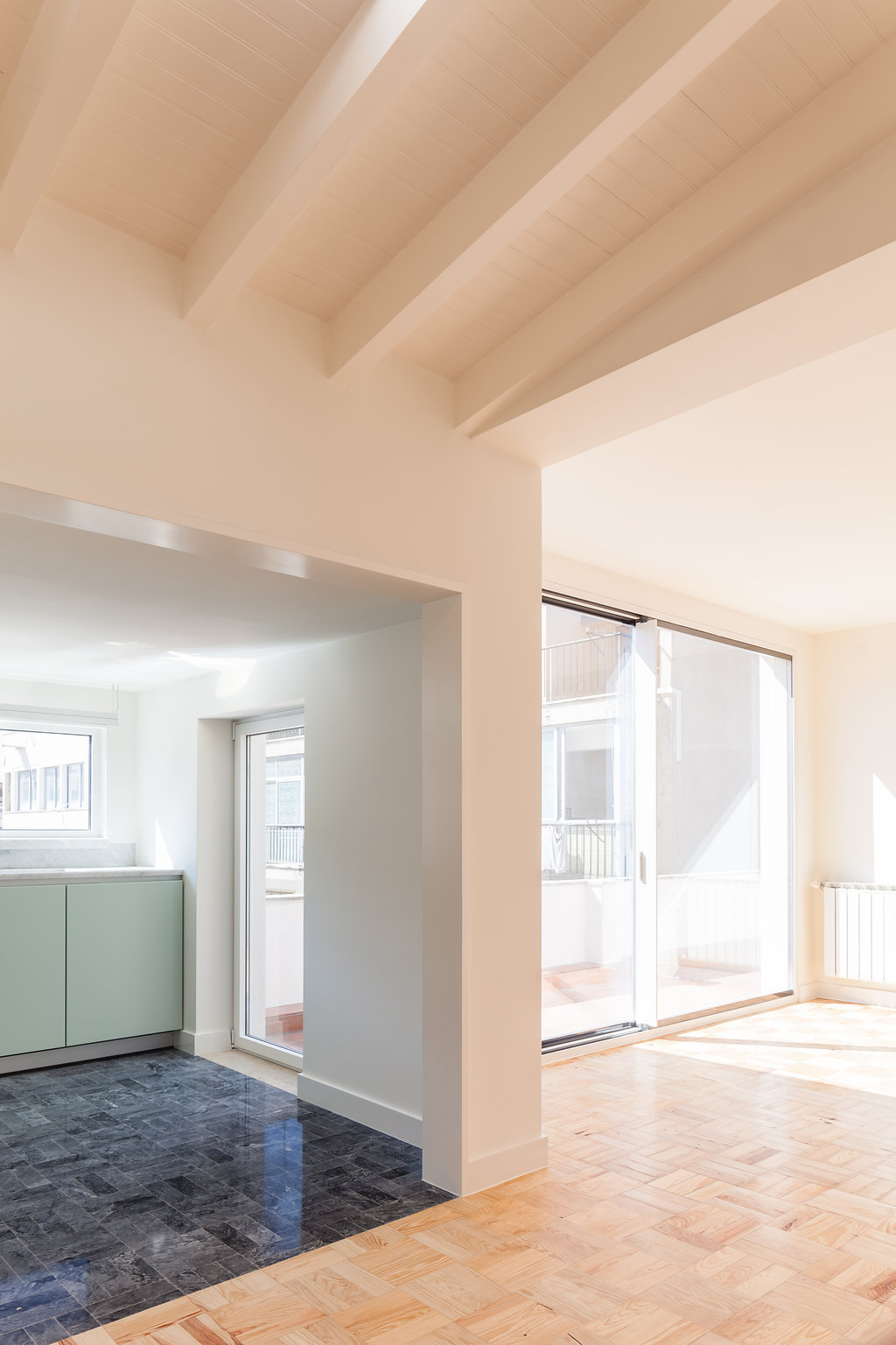 Open living area with white timber ceiling beams, herringbone pine floor and a sliding glass door in bright afternoon sun