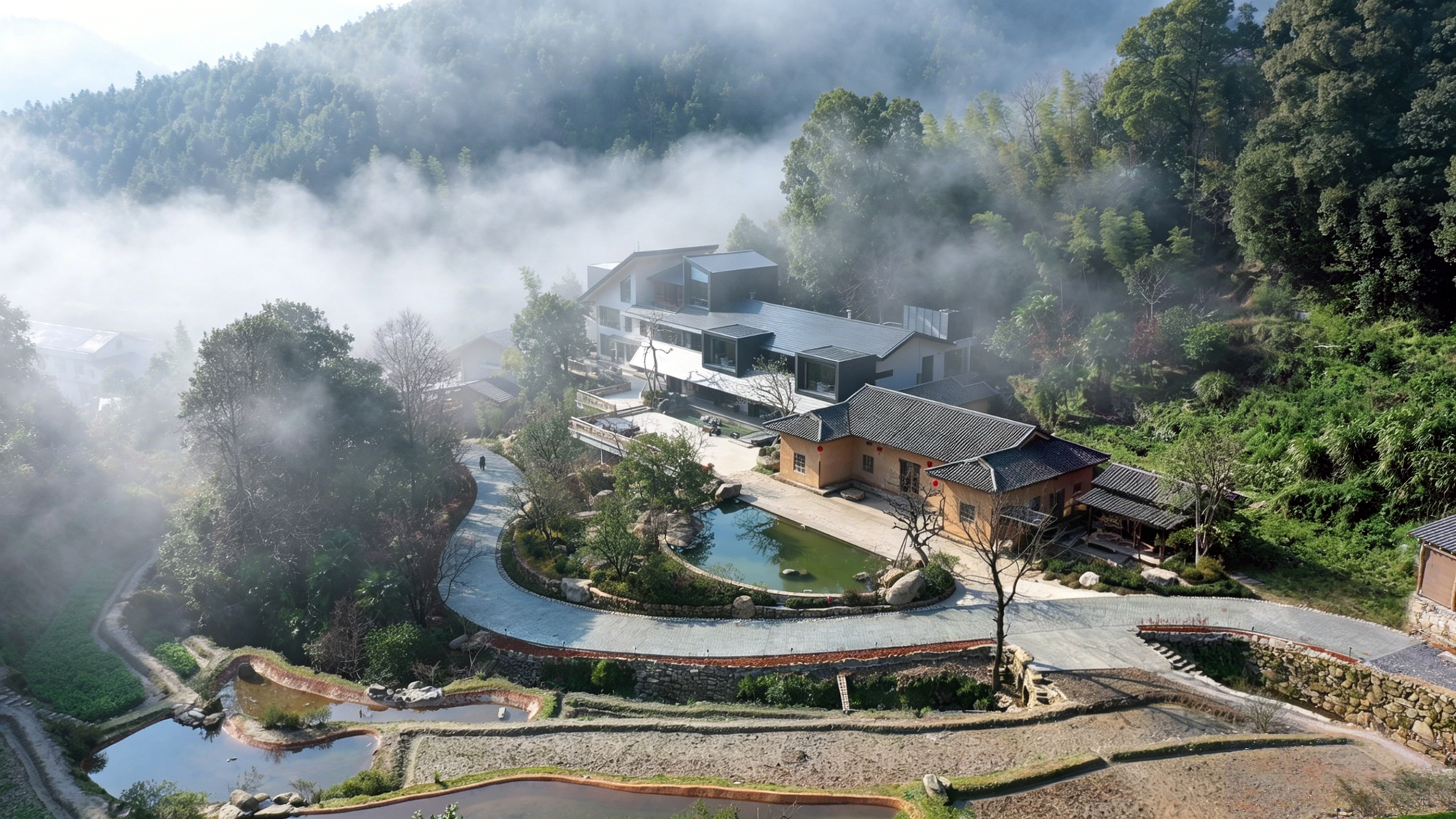 Aerial view of terraced rice paddies and curved pathways wrapping around multiple buildings in morning mist
