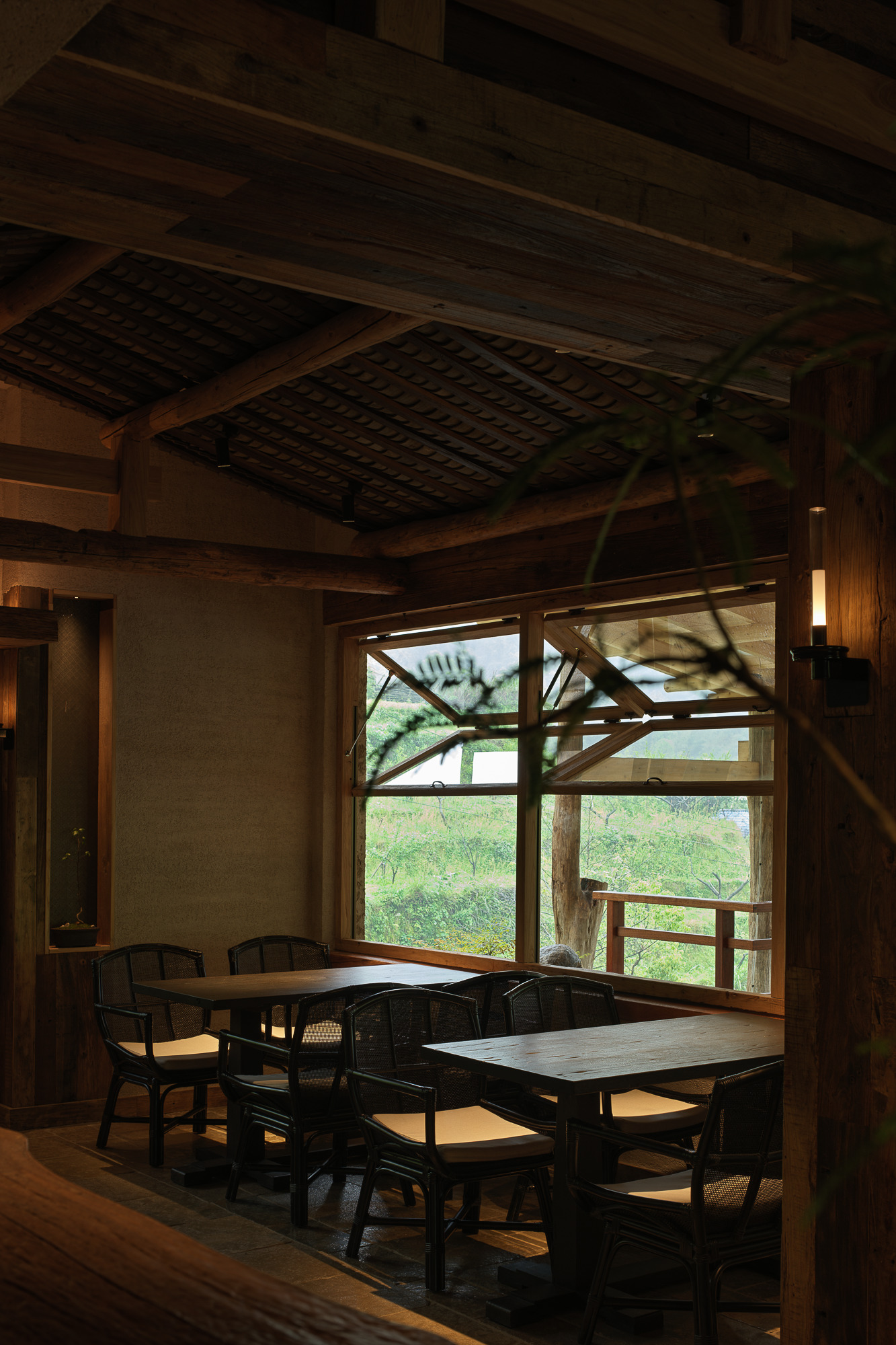 Interior dining area with timber ceiling beams and large window framing views of a terrace and greenery