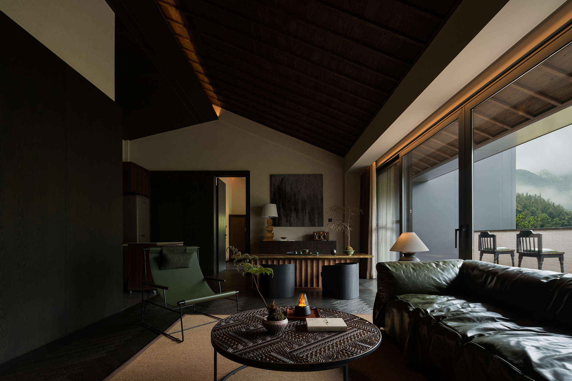 Living room with dark timber ceiling and glazed doors opening to a terrace with misty mountain views