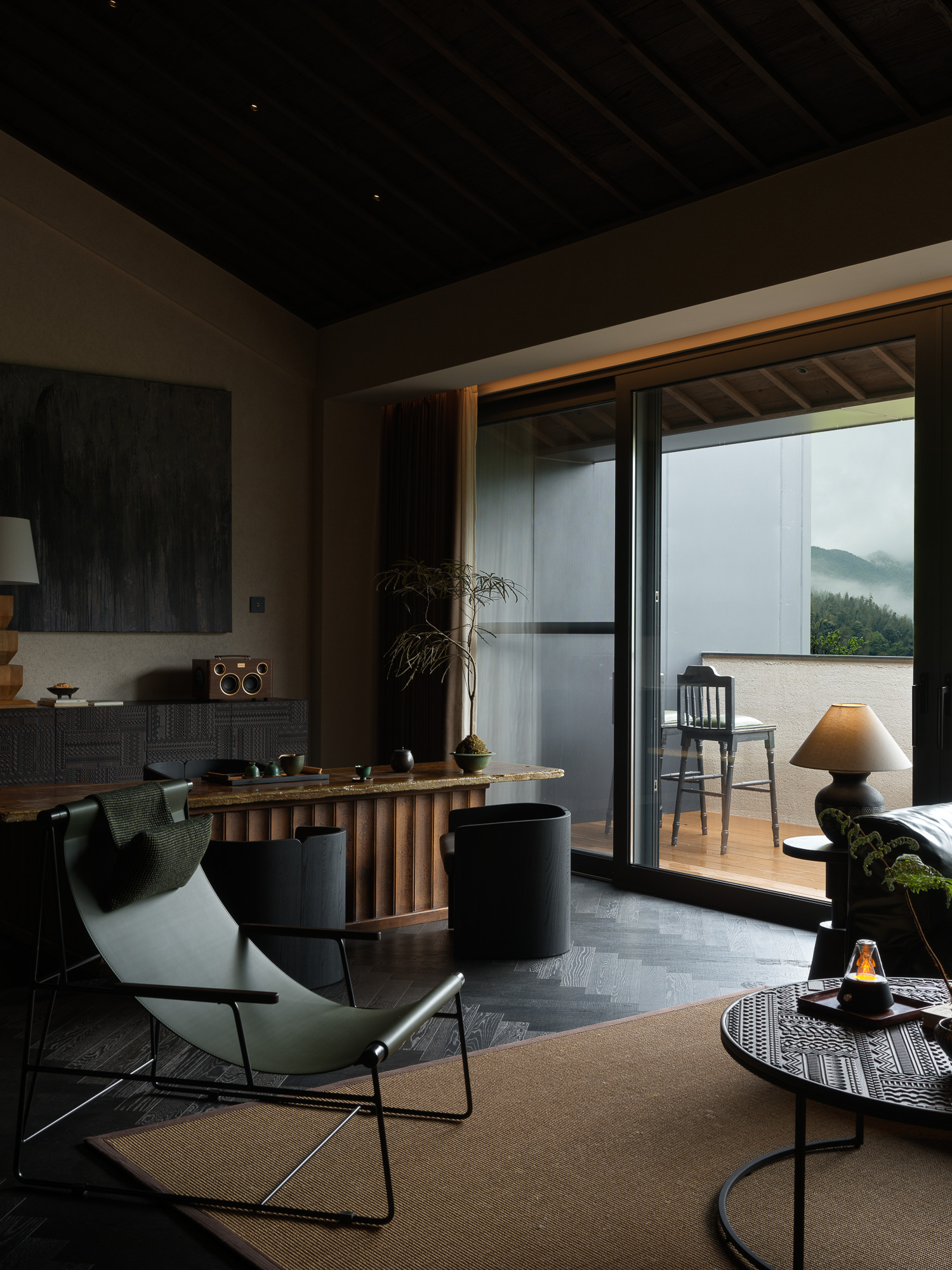 Open living space with fluted timber bar and sliding glass doors framing forested mountains in fog