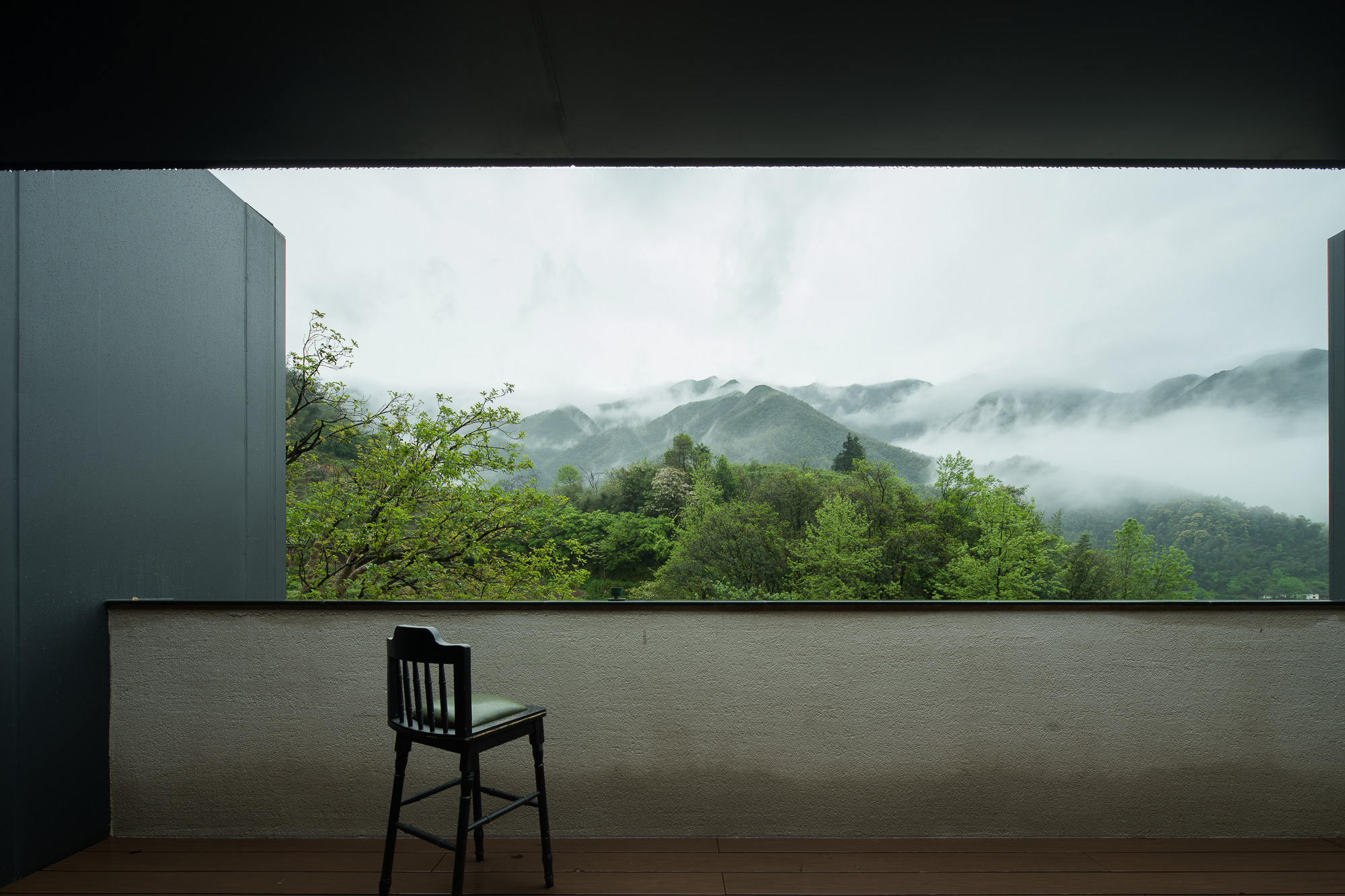 Outdoor terrace with single chair facing cloud-wrapped mountains and dense green forest below