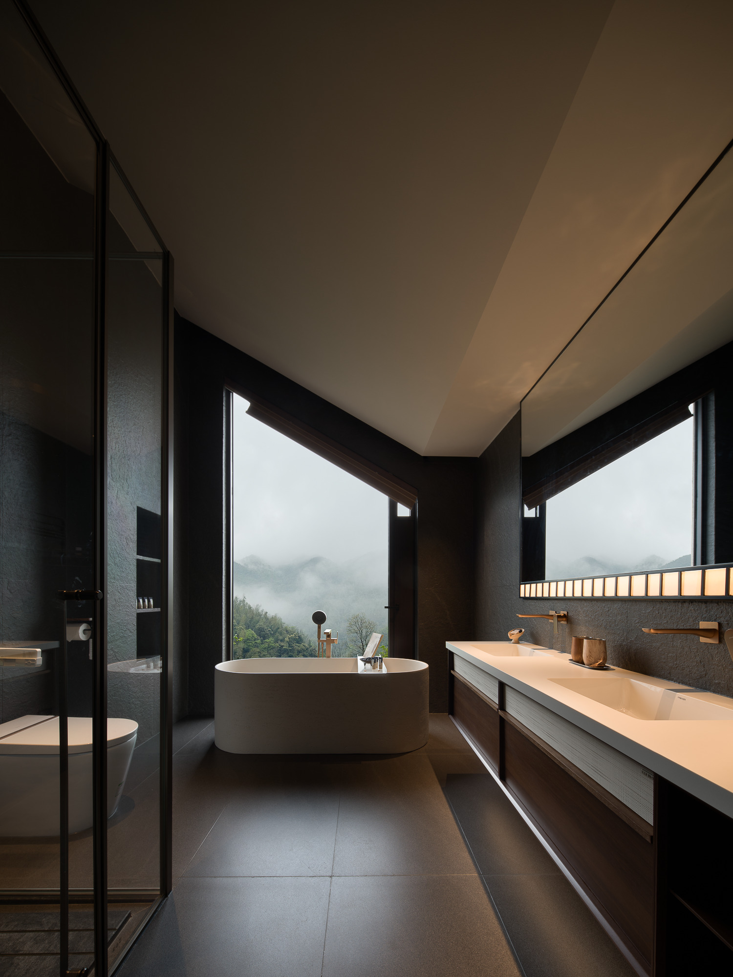 Bathroom with freestanding tub and corner windows overlooking misty hills under an overcast sky