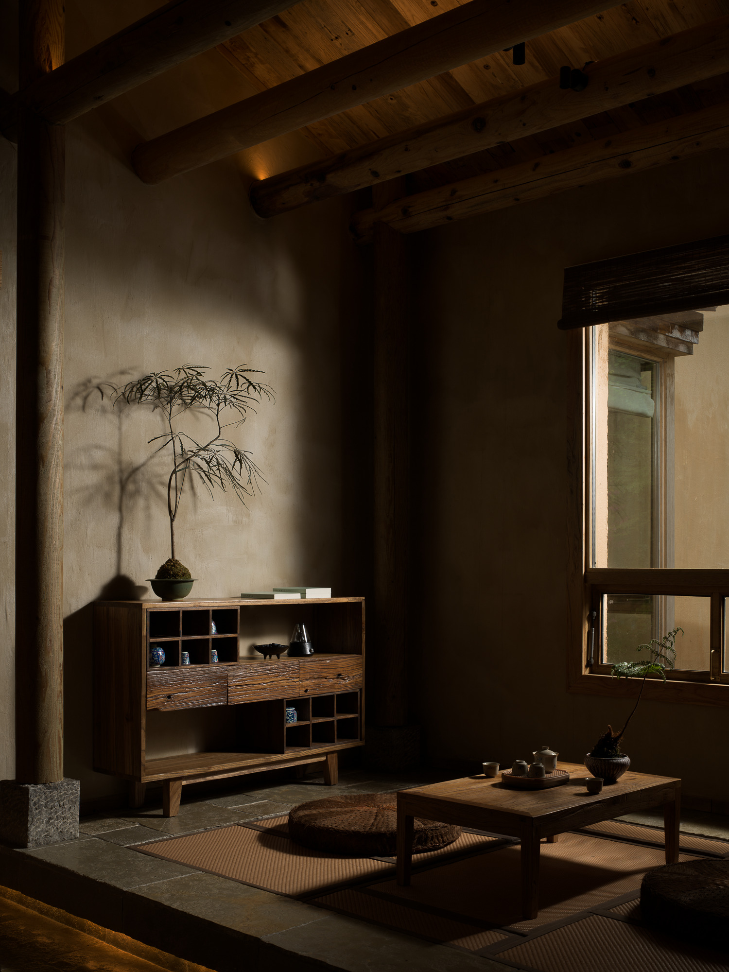Sunlit interior room with exposed timber beams, low table on tatami mats and a potted plant