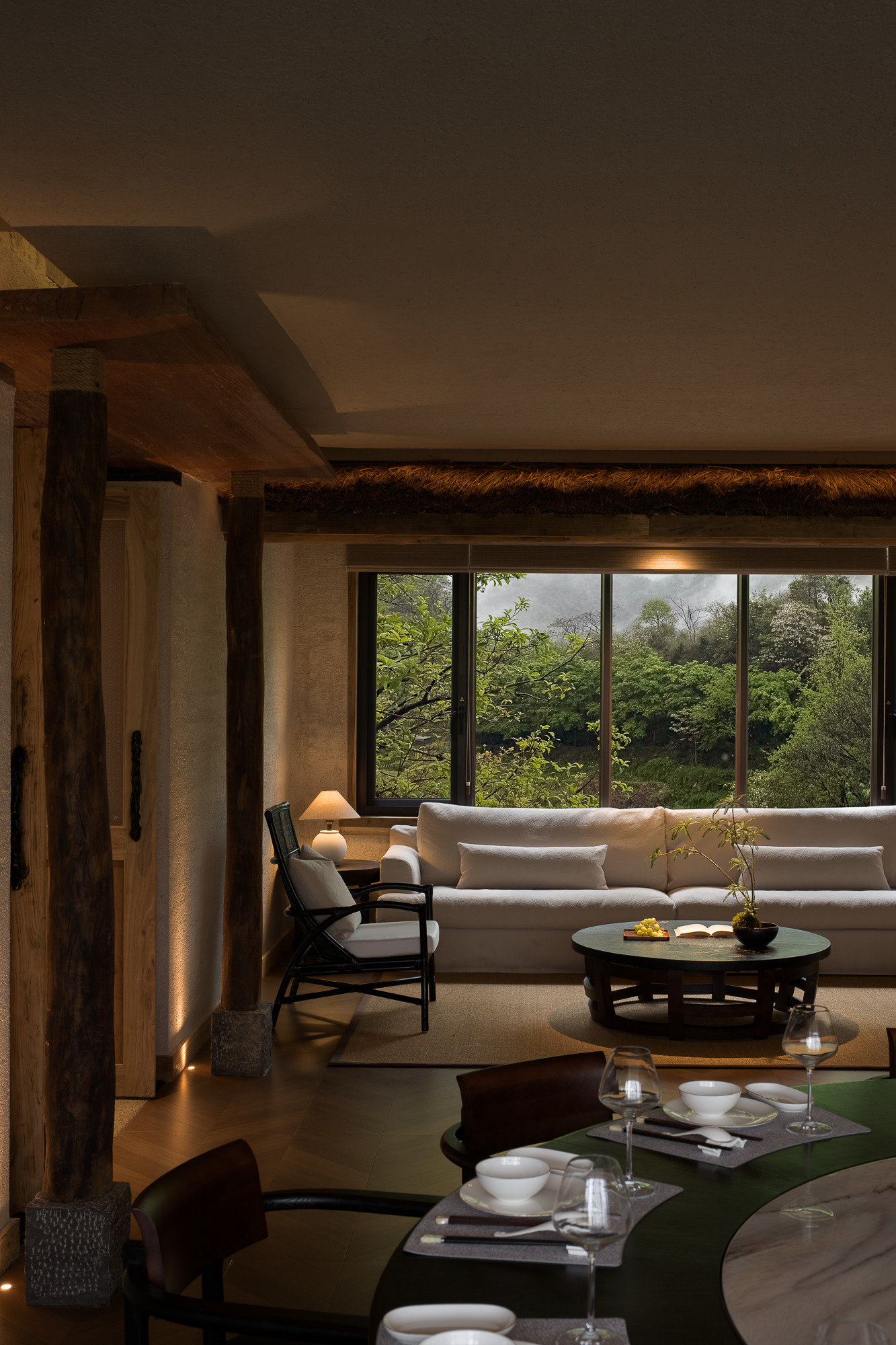 Living space with floor-to-ceiling glazing framing dense forest beyond timber columns