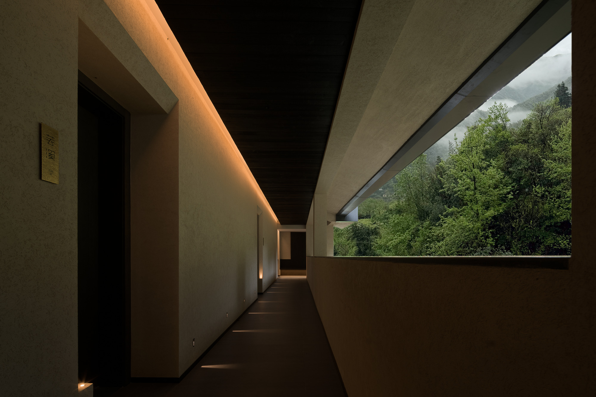 Interior corridor with cove lighting along the ceiling and a horizontal window framing lush green hillside