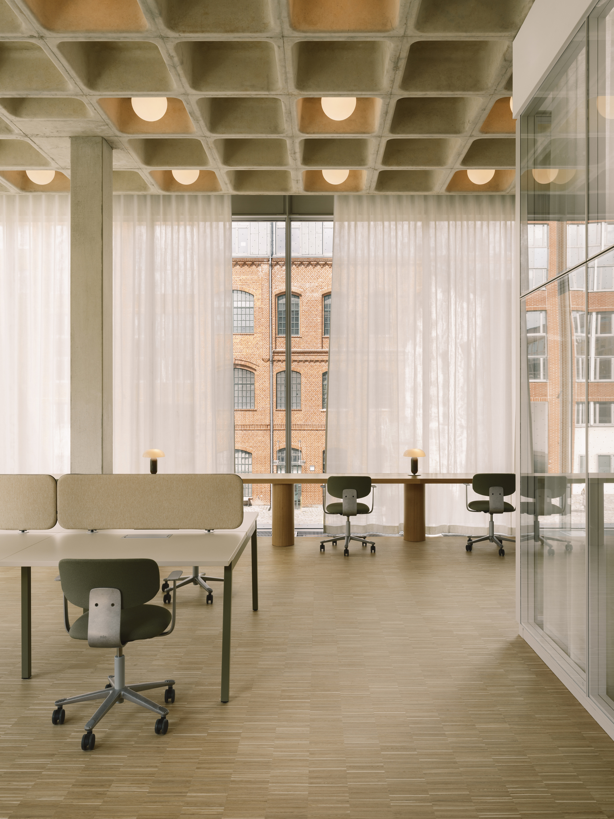 Open office floor with concrete waffle ceiling, sheer curtains filtering daylight and views to brick facade