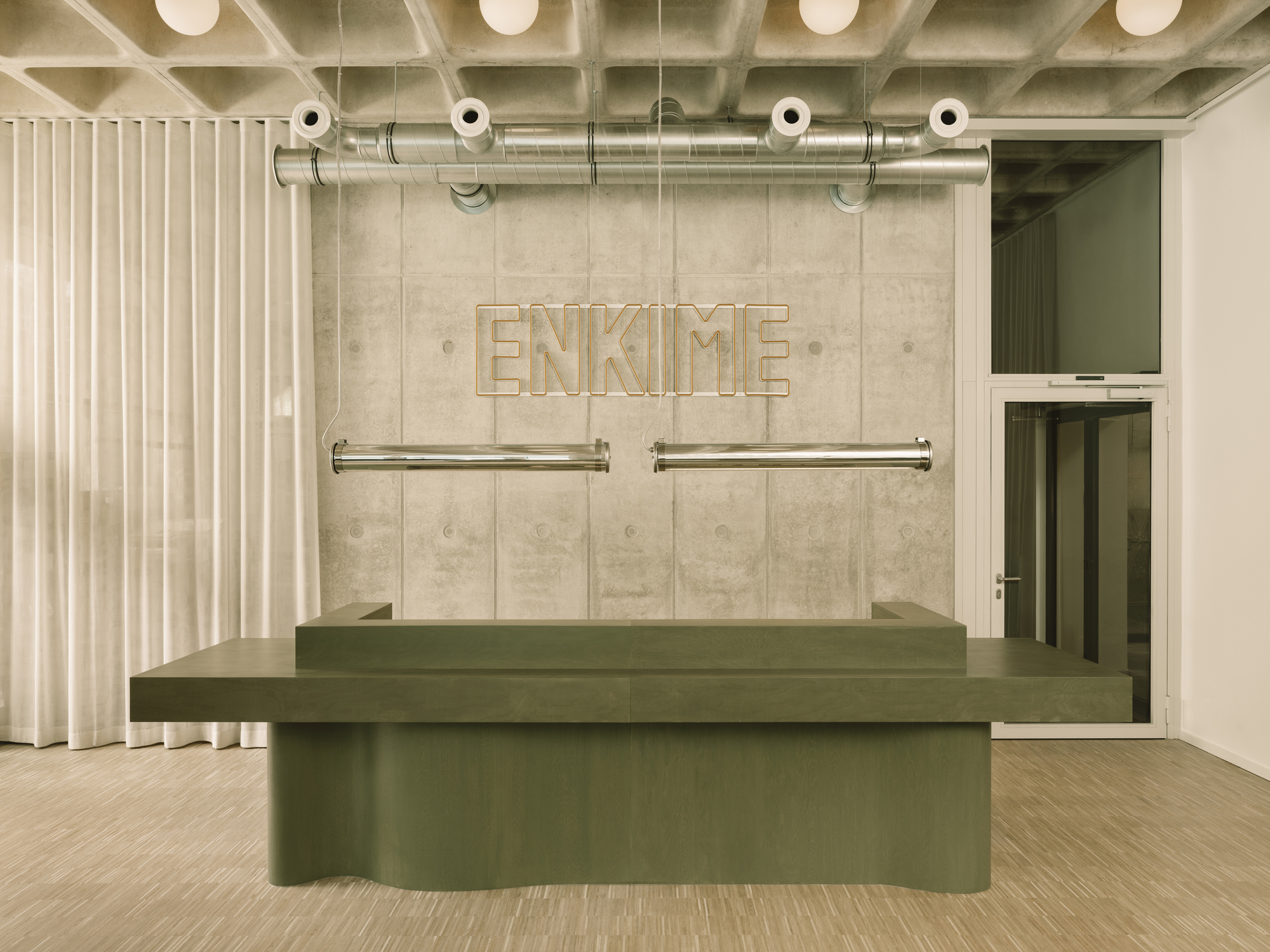 Reception desk with paneled concrete wall displaying dimensional lettering and exposed ceiling ductwork