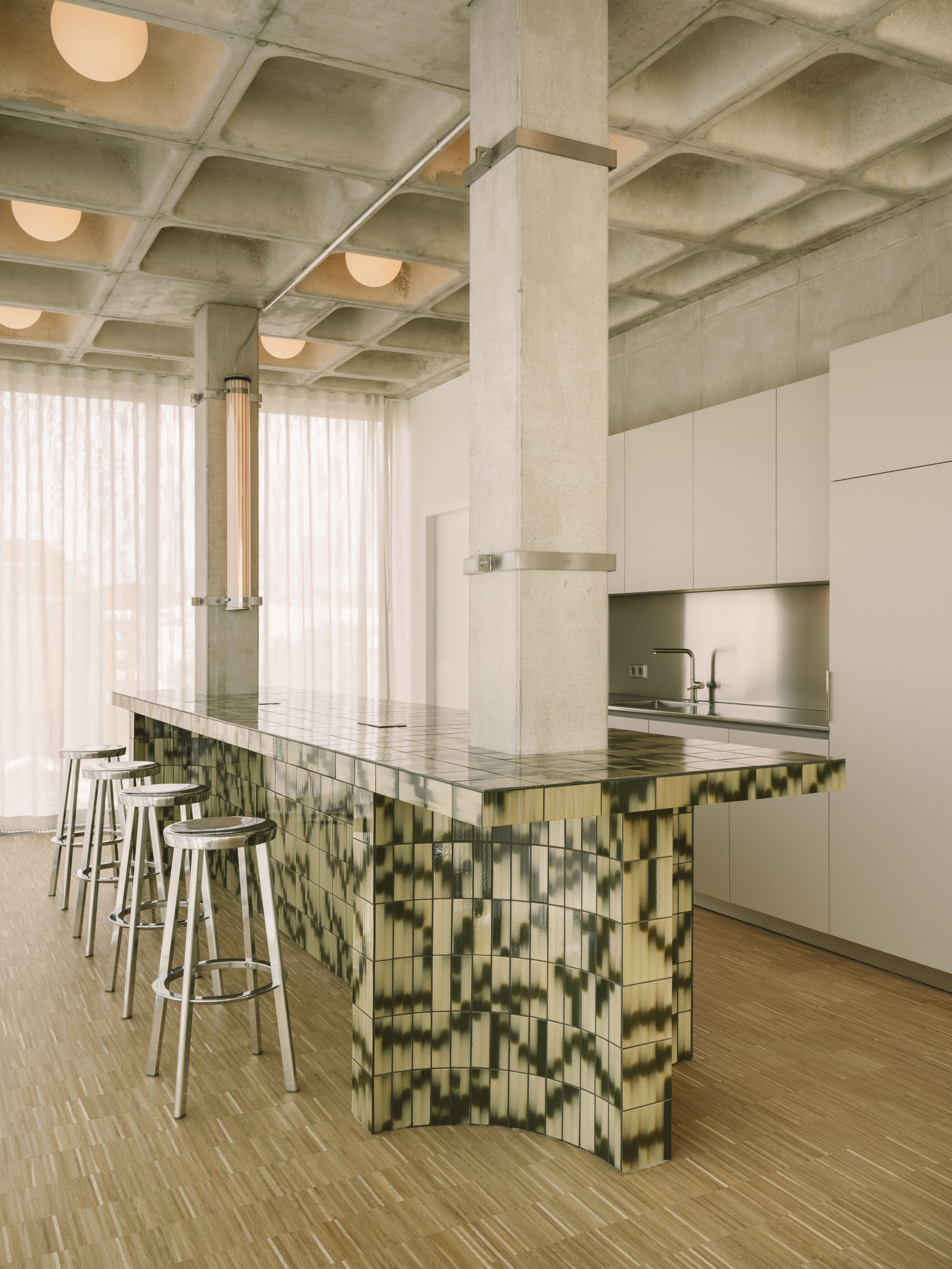 Kitchen island with green glazed tile base and white upper cabinets beneath concrete waffle ceiling