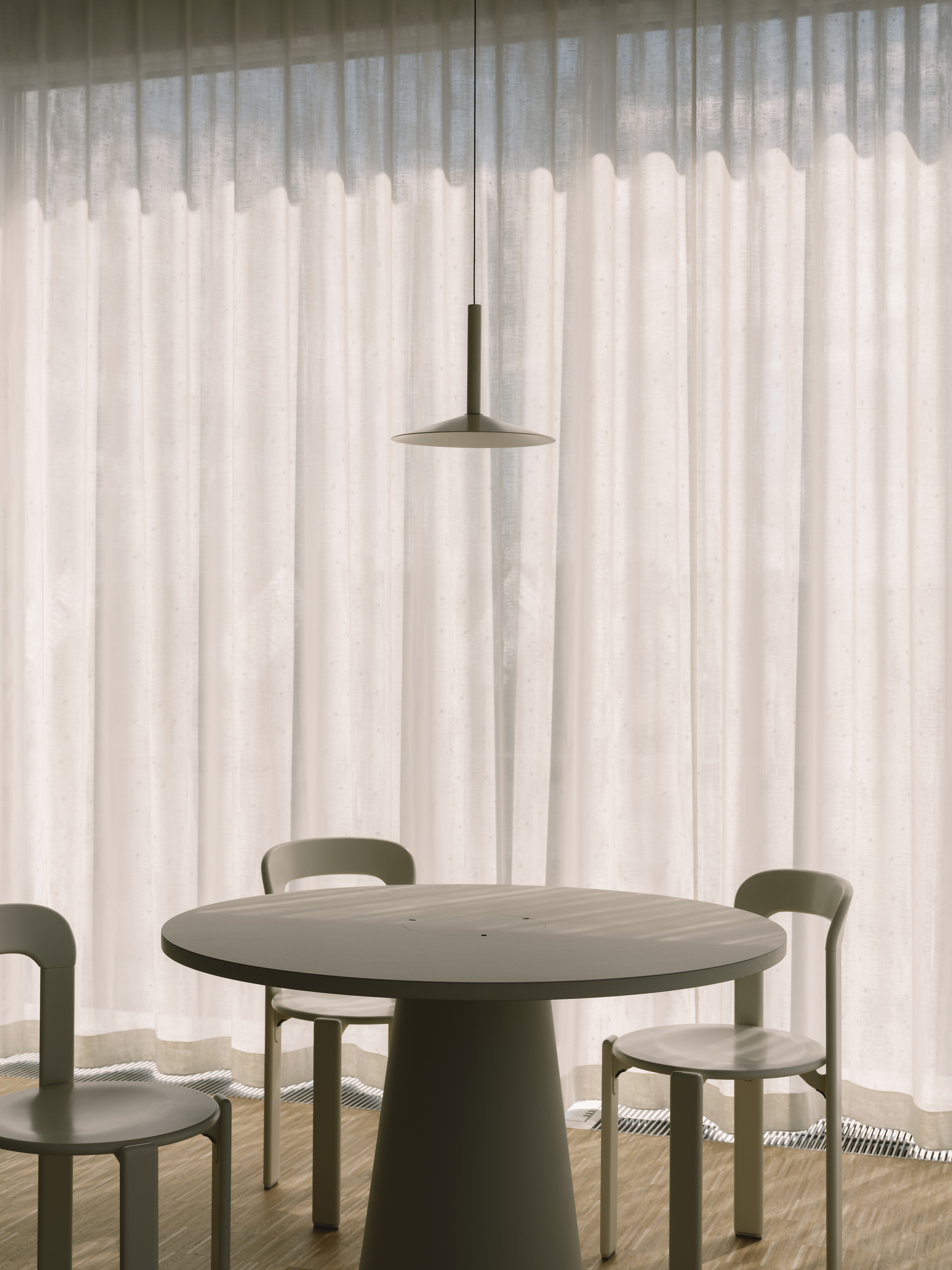 Round dining table with pendant light suspended above translucent curtains filtering afternoon sun