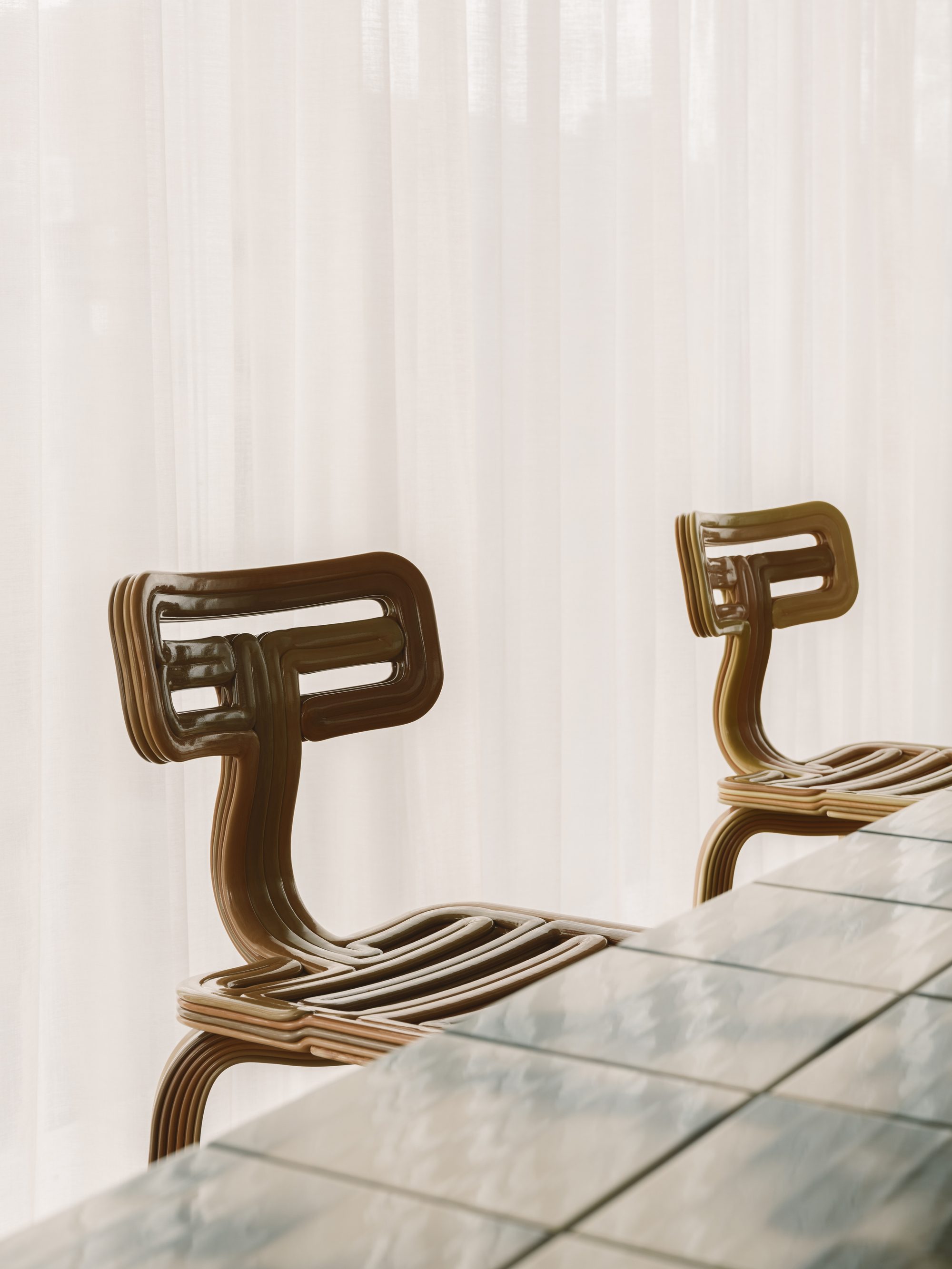 Close-up of two laminated plywood chairs with curved backs beside glass table surface