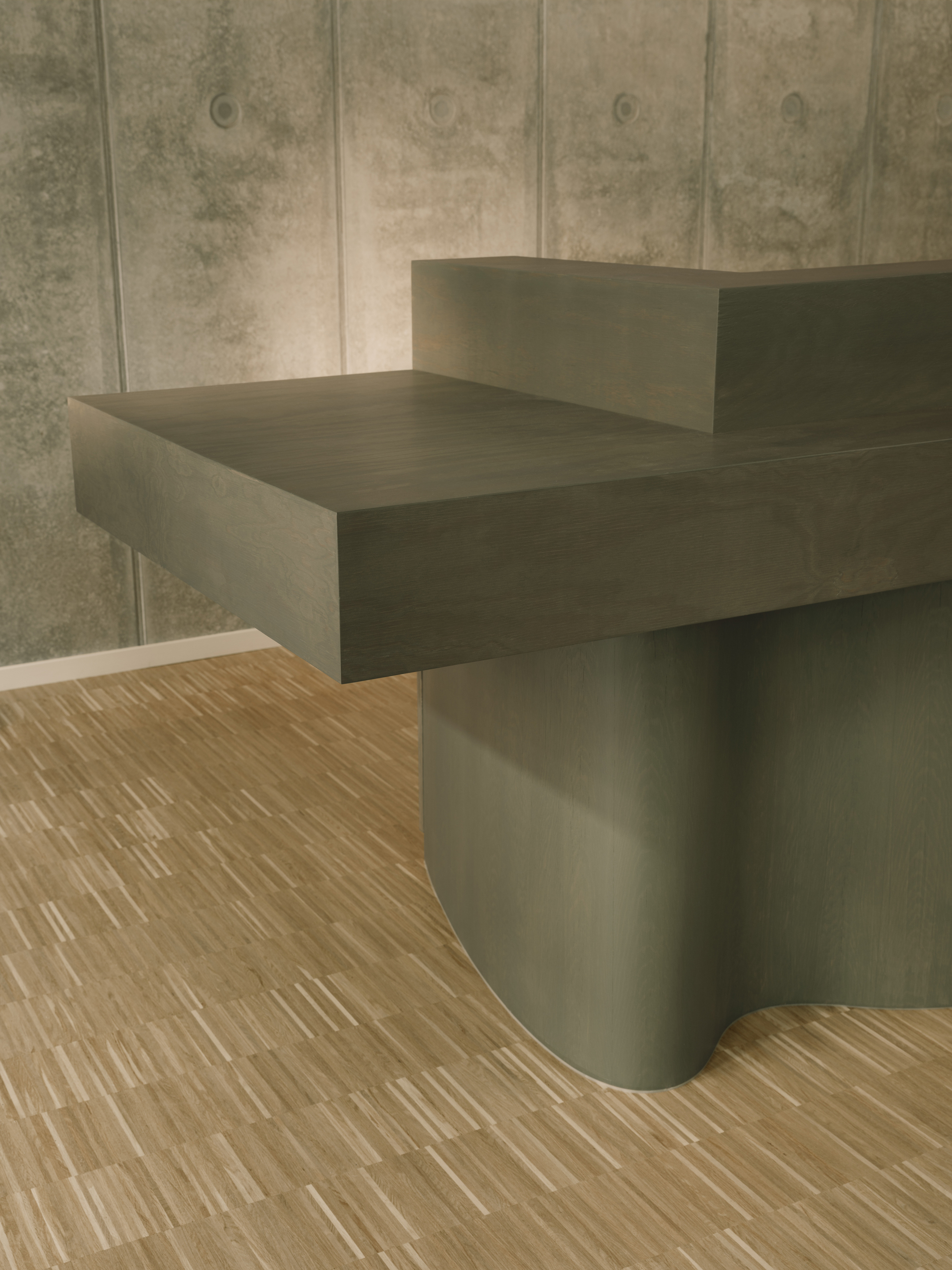 Reception desk with curved base meeting wood flooring against board-formed concrete wall
