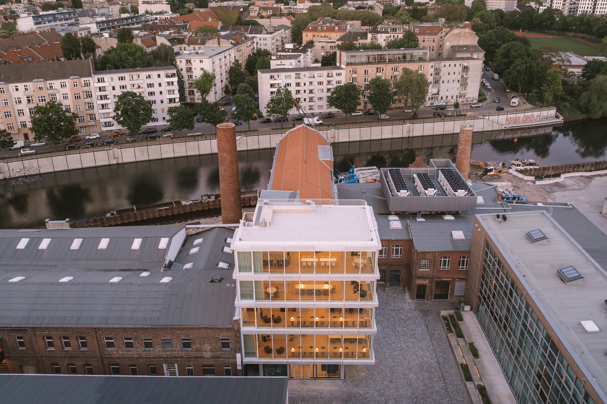 Aerial view of the five-story glazed volume inserted among brick warehouses and residential blocks beside the river