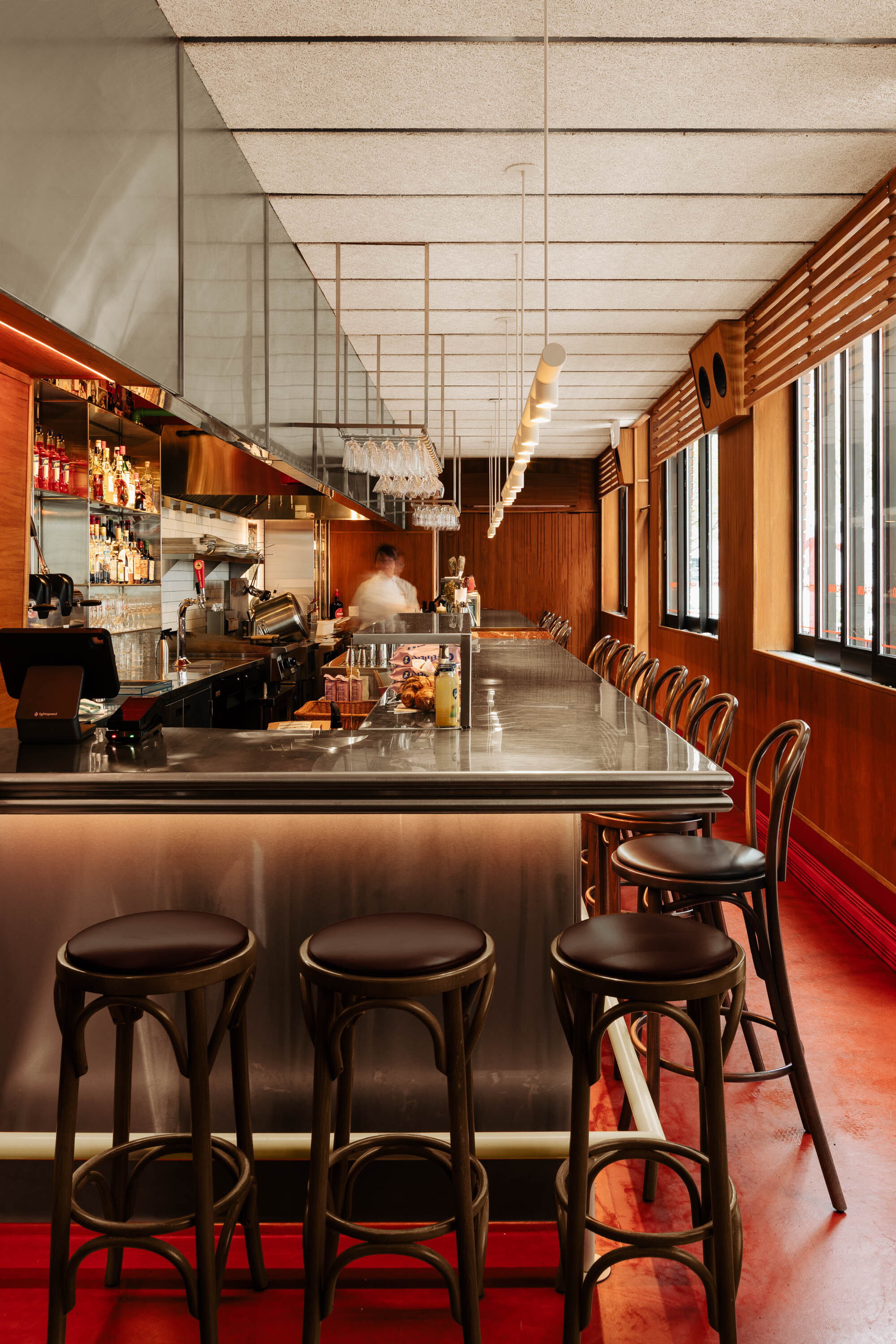 Illuminated bar counter with bentwood stools and wood paneling along the window wall with sunlight