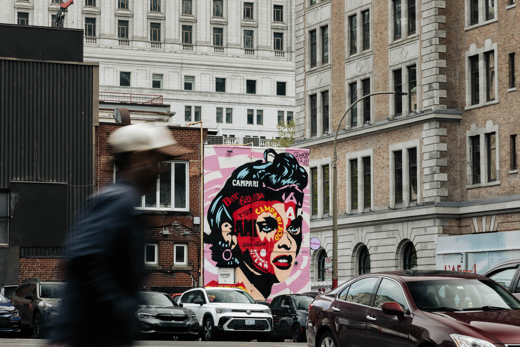 Street view with a figure in motion passing a mural on a building facade