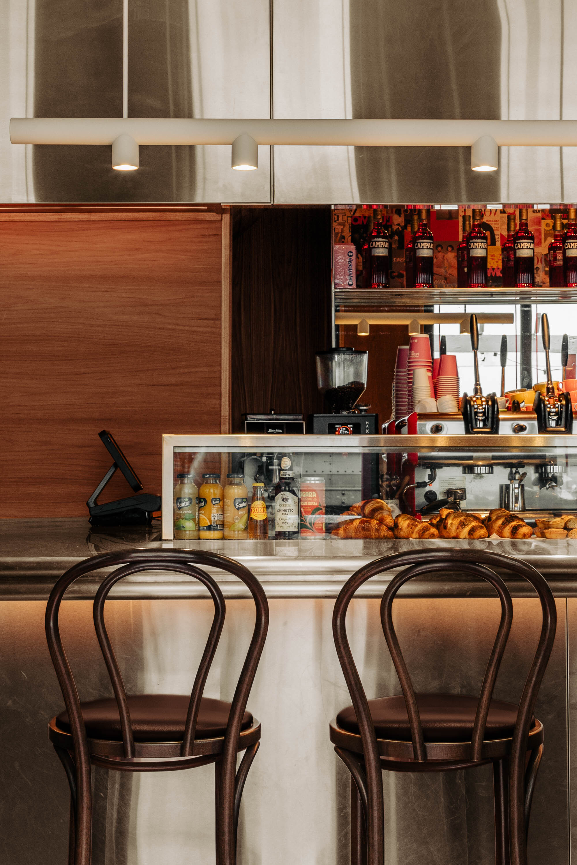 Glass pastry display case with bentwood chairs at a counter under linear pendant lights