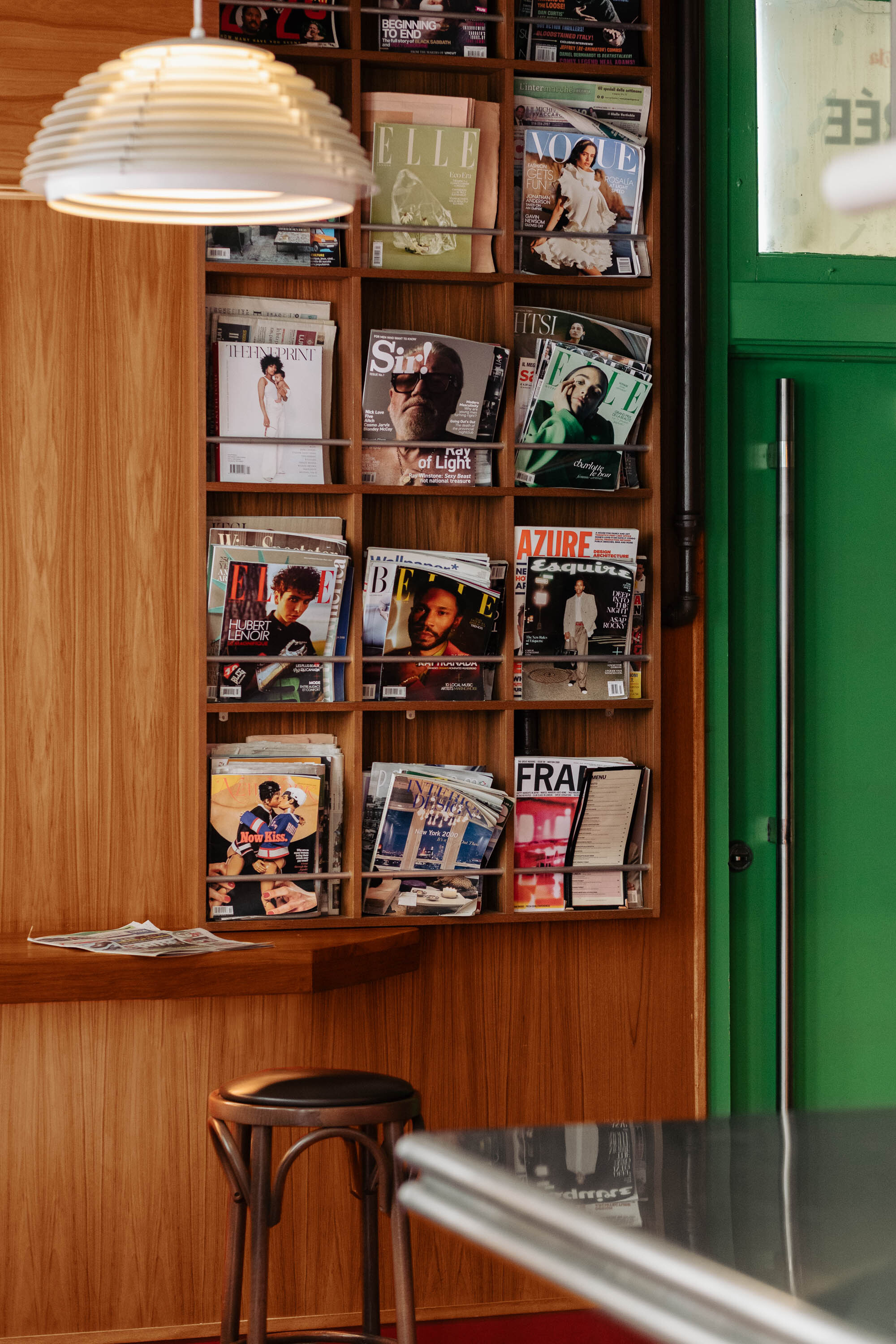 Timber wall-mounted magazine rack with pendant lamp beside a green painted door
