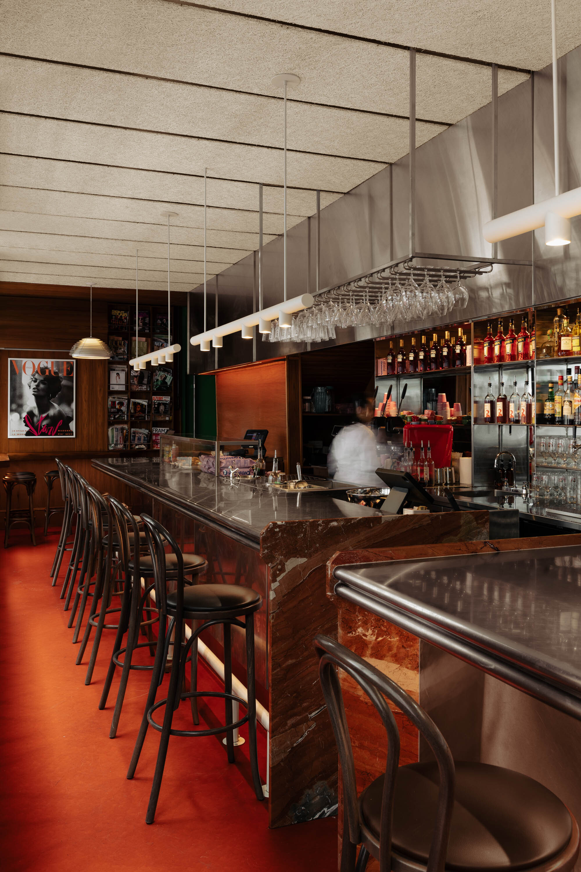 Bar interior with overhead glassware rack and figure working behind the counter at night