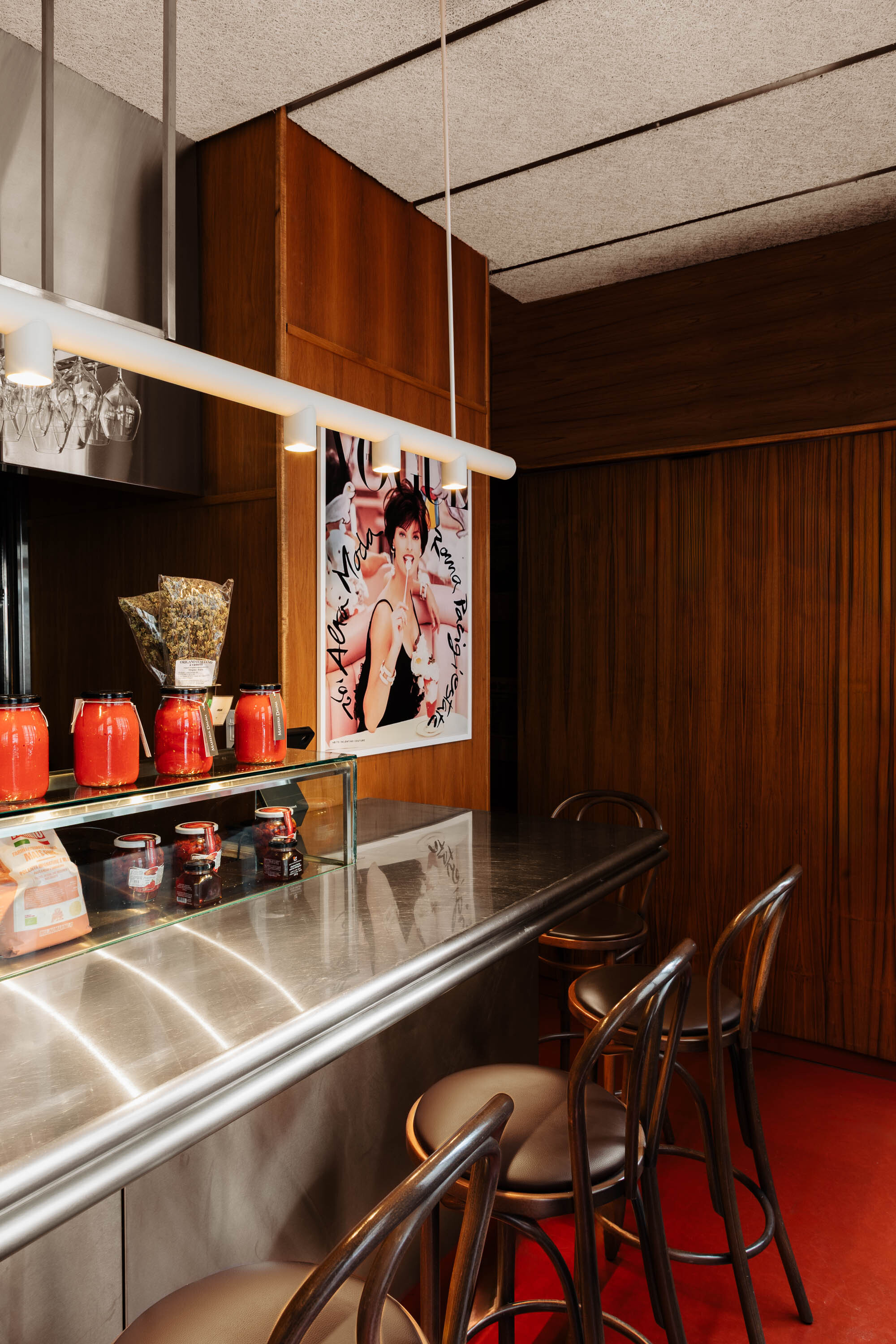 Bar counter with stainless steel front, walnut paneling and bentwood stools on red rubber flooring