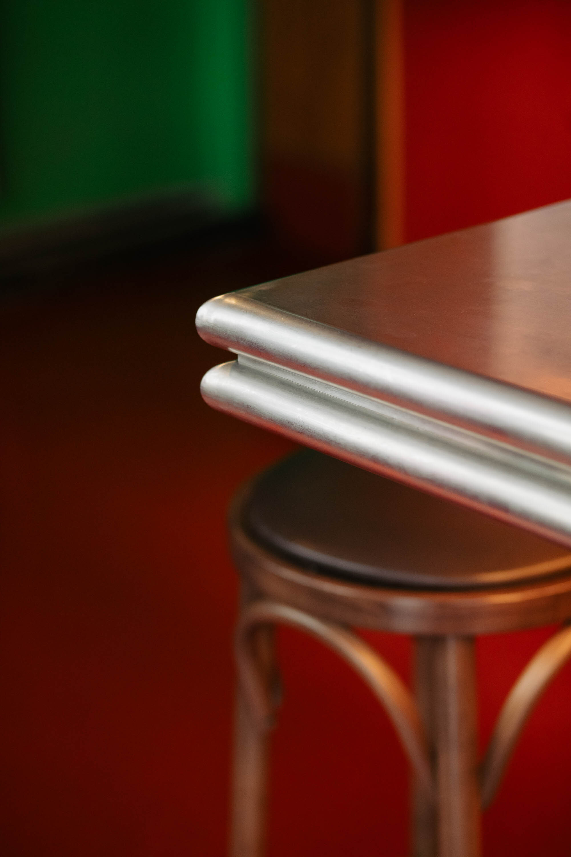 Close-up of rounded stainless steel counter edge meeting a bentwood stool against red floor