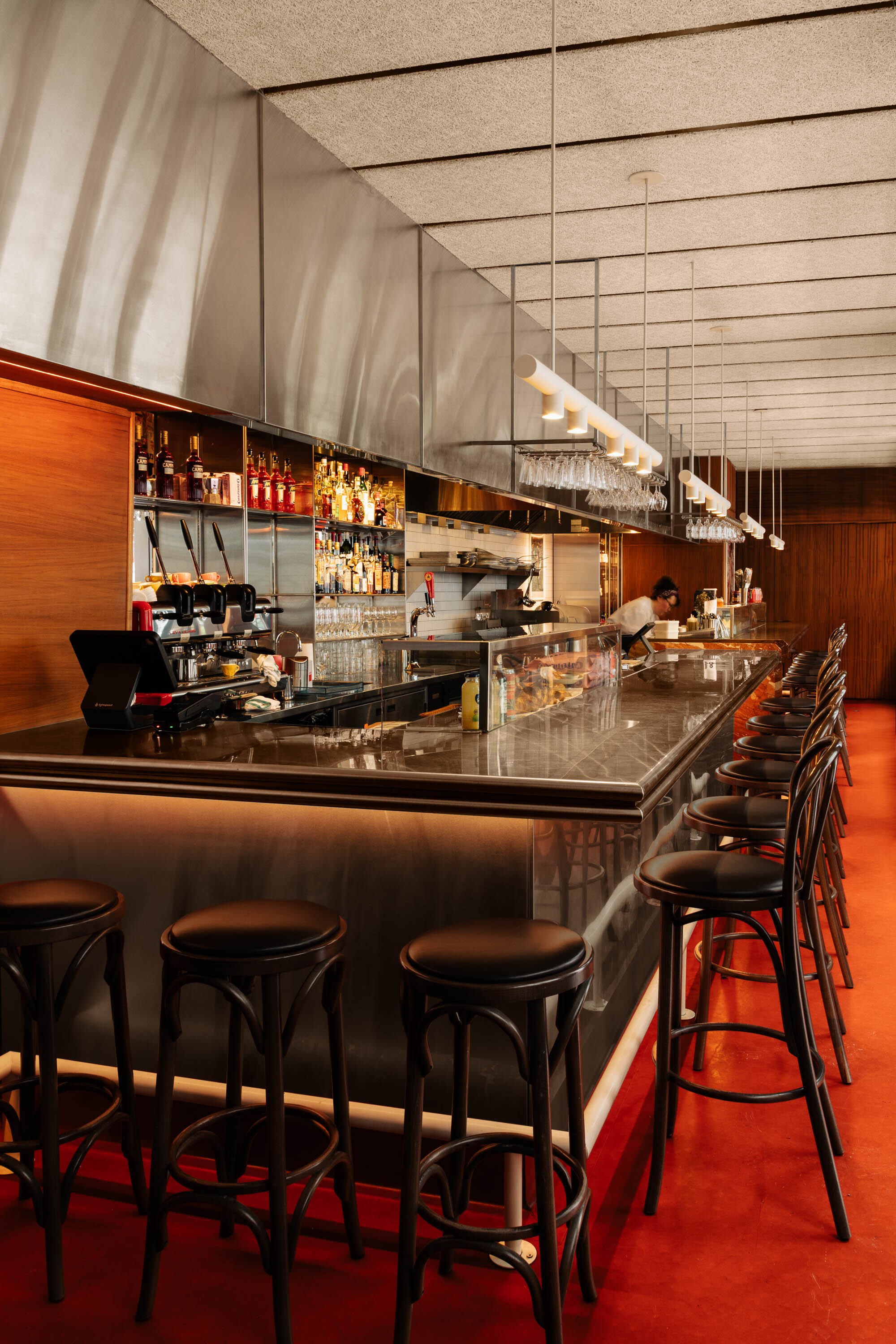 Long view of the bar with stainless counter, suspended tubular lights and textured ceiling