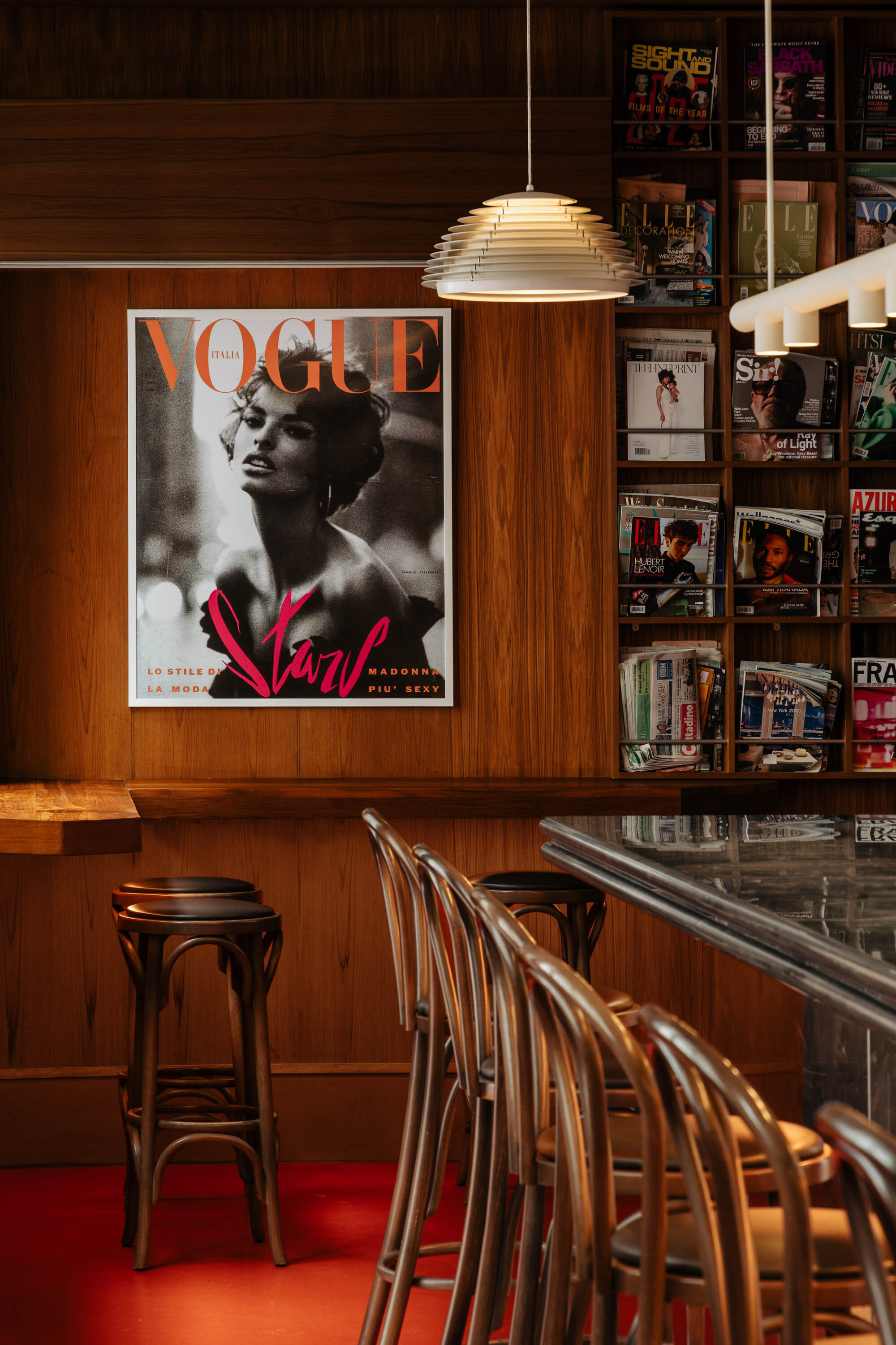 Timber-paneled bar area with bentwood stools, layered pendant light and magazine display under warm lighting