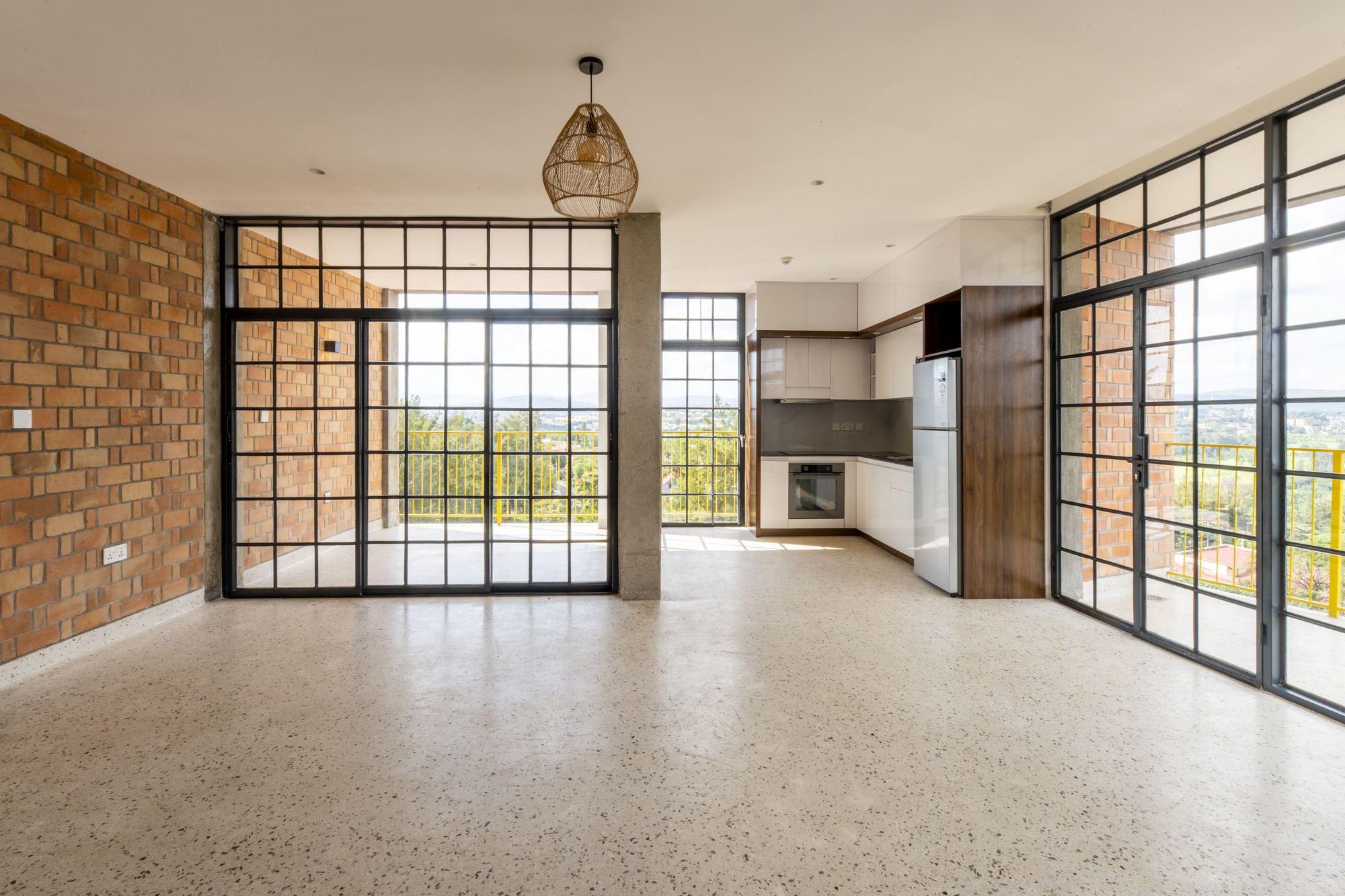 Open-plan interior with exposed brick wall, steel-framed glazed doors, terrazzo floor and compact kitchen