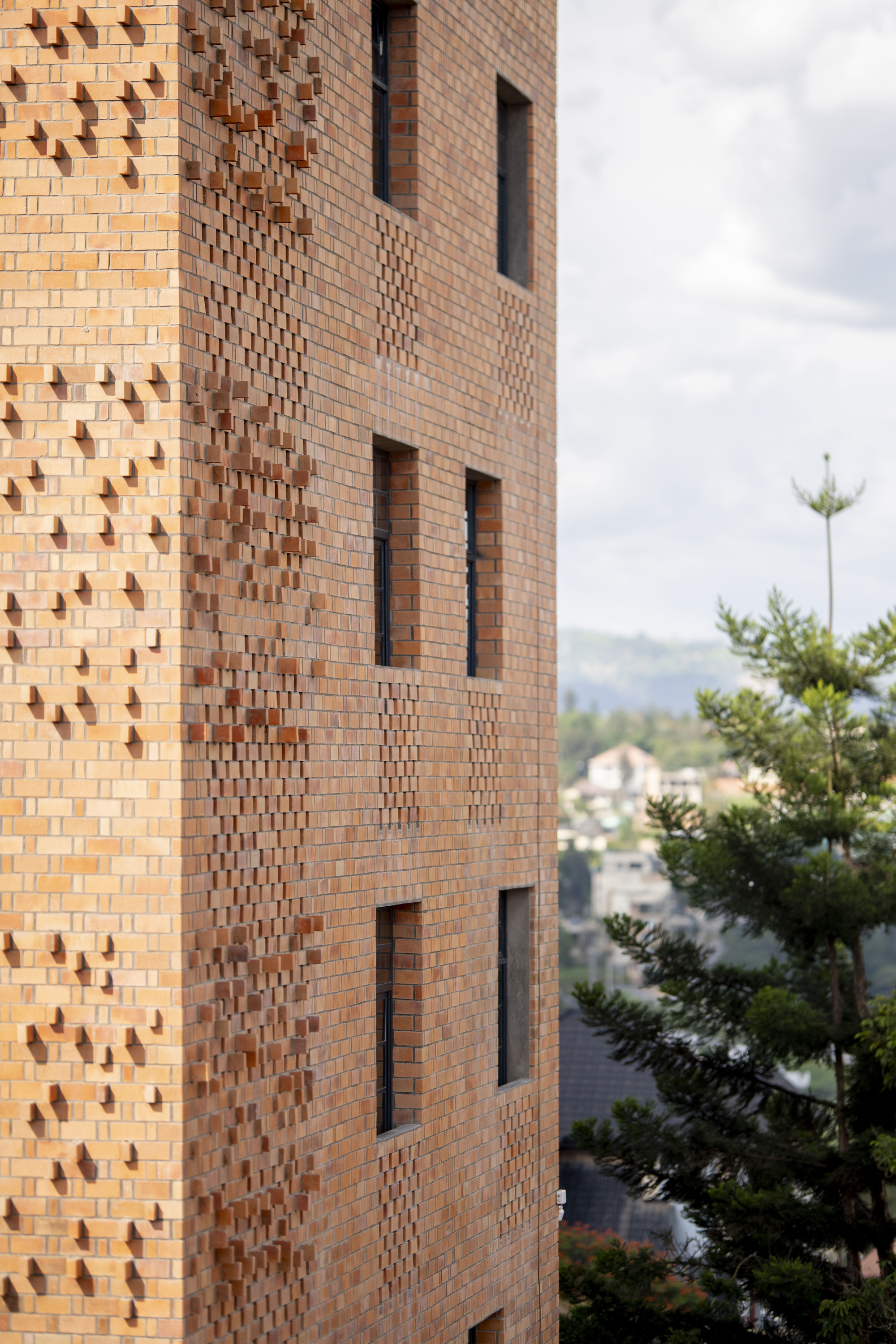Facade detail showing patterned brickwork with protruding headers and recessed window openings beside green trees