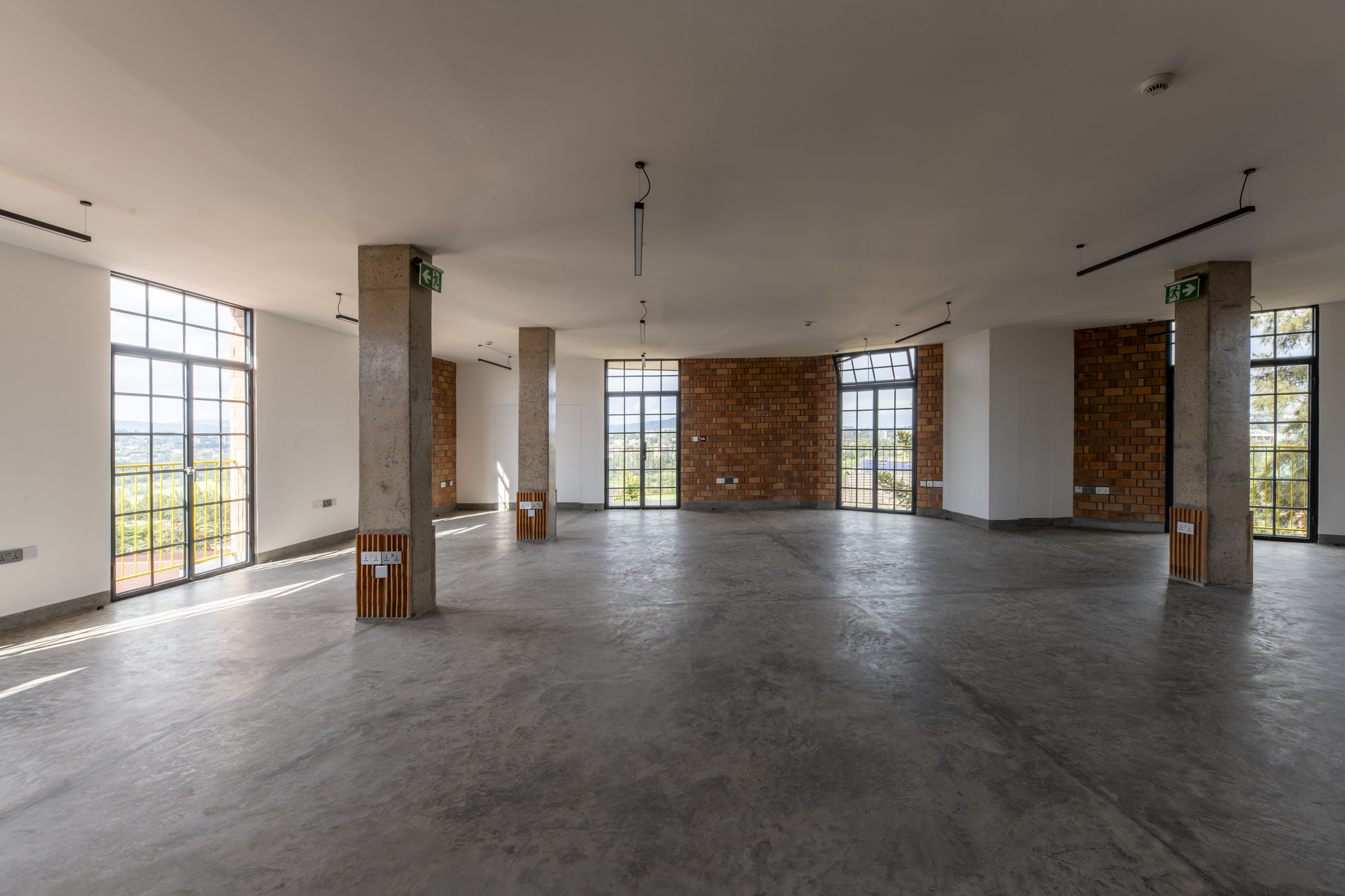 Open floor plan with polished concrete floor, concrete columns and metal-framed windows overlooking green landscape
