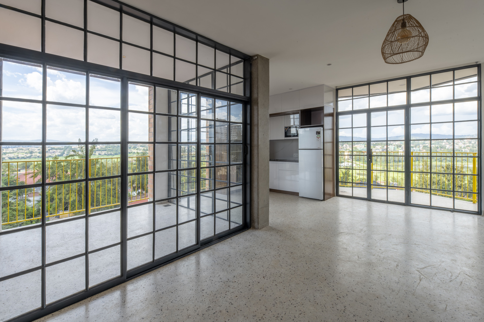 Living area with black-framed glass partition wall and floor-to-ceiling windows opening to terrace with yellow railing
