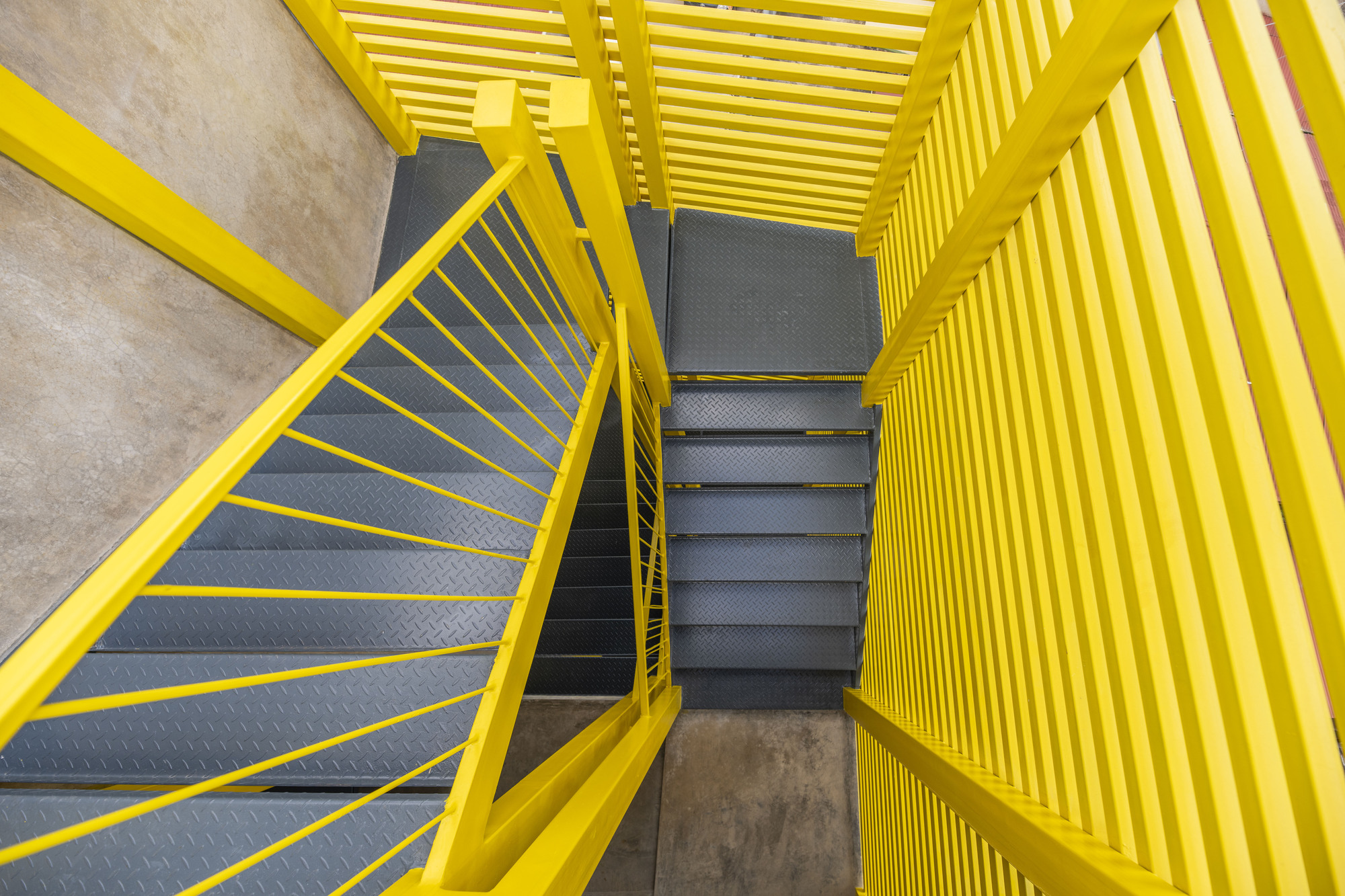 Top-down view of the yellow steel staircase with black treads enclosed by vertical louver screens