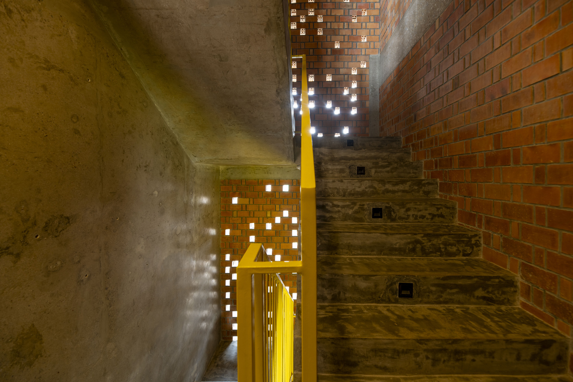 Interior stairwell with patterned brick screen wall casting light through perforations at dusk