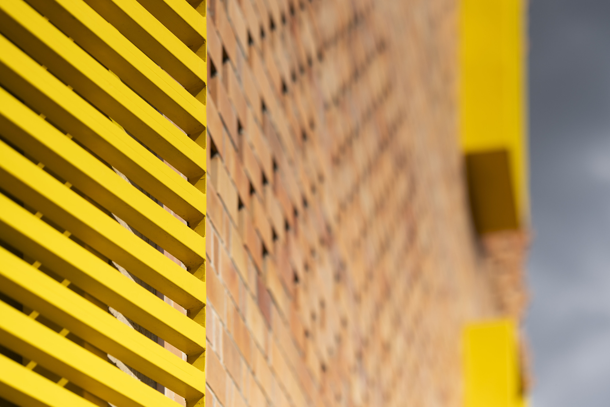 Detail of yellow horizontal louvres meeting a perforated brick wall with yellow accents