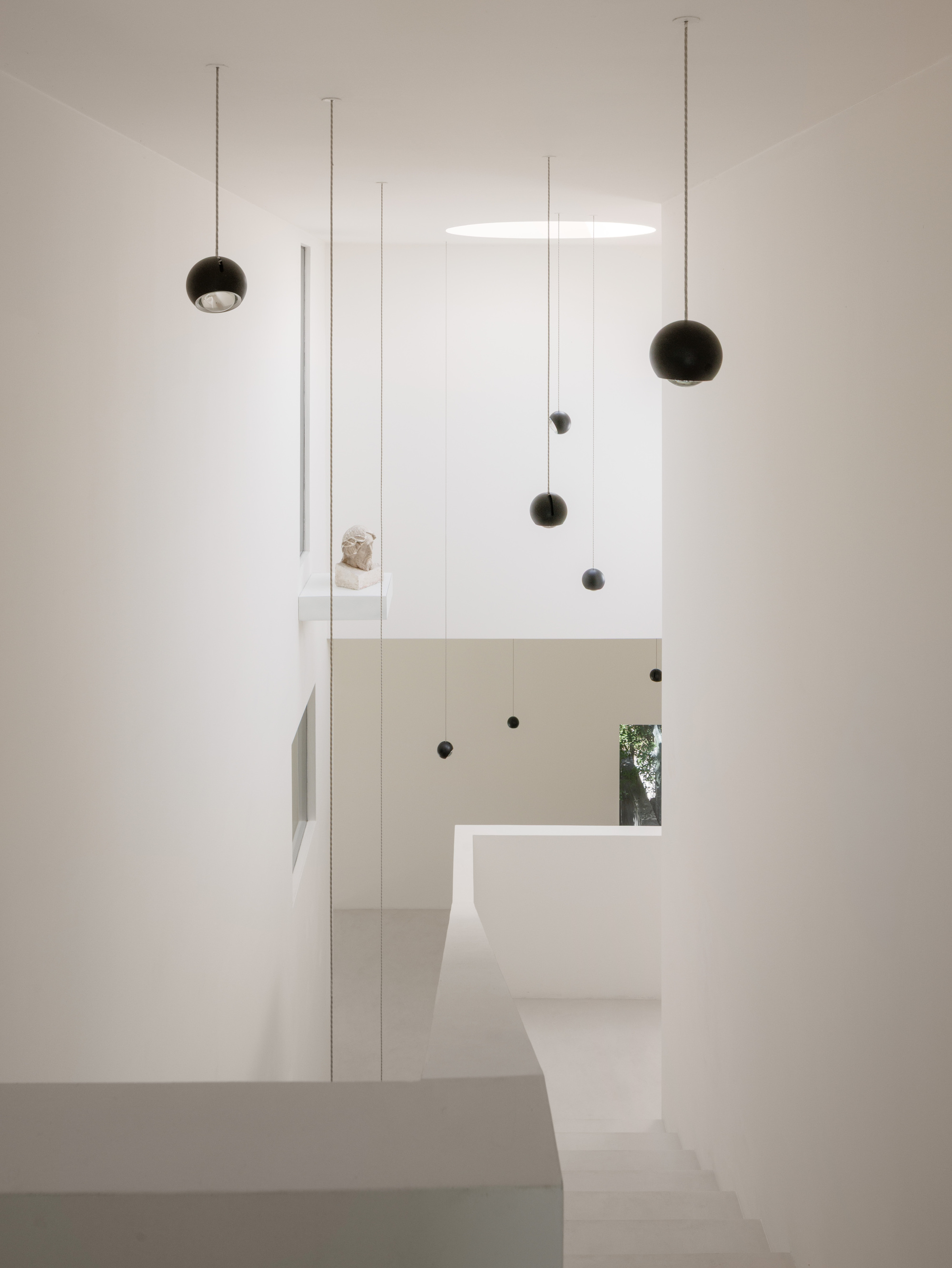 White double-height stairwell with suspended spherical pendant lights and narrow window glimpse