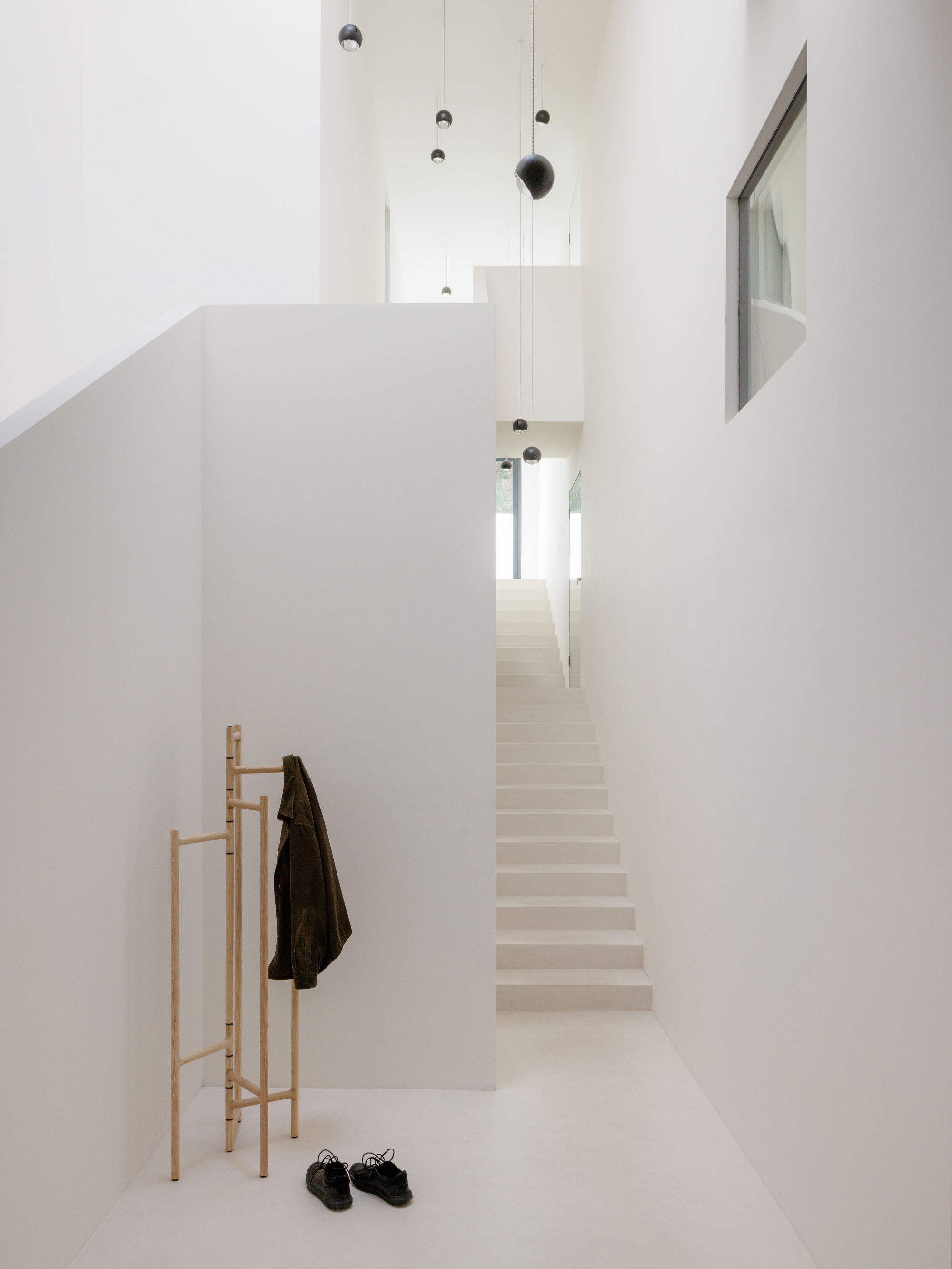 White entry hall with timber coat stand and pale staircase ascending under suspended pendant lights