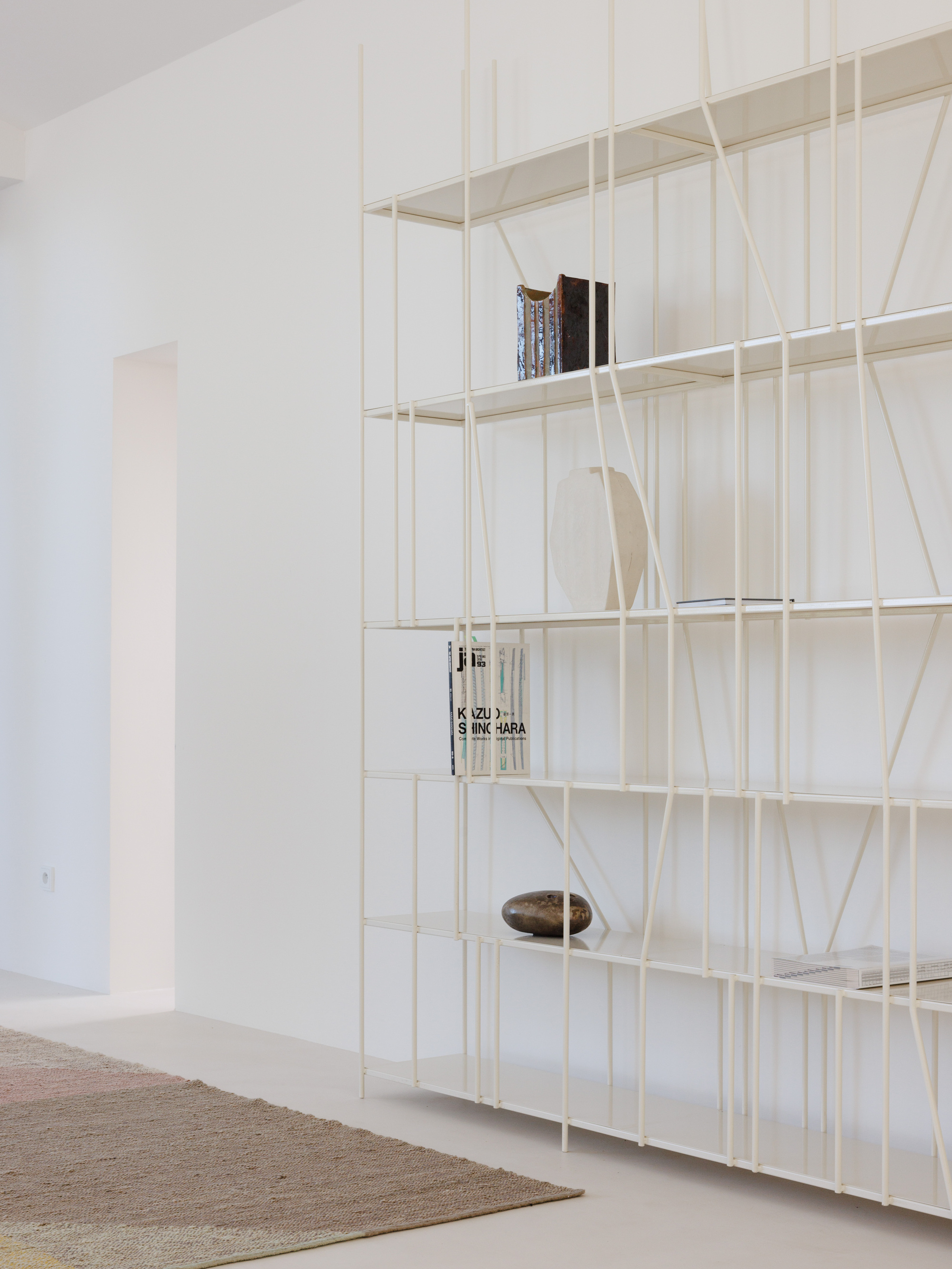 Detail of cream wire grid shelving system holding books and objects against a white wall