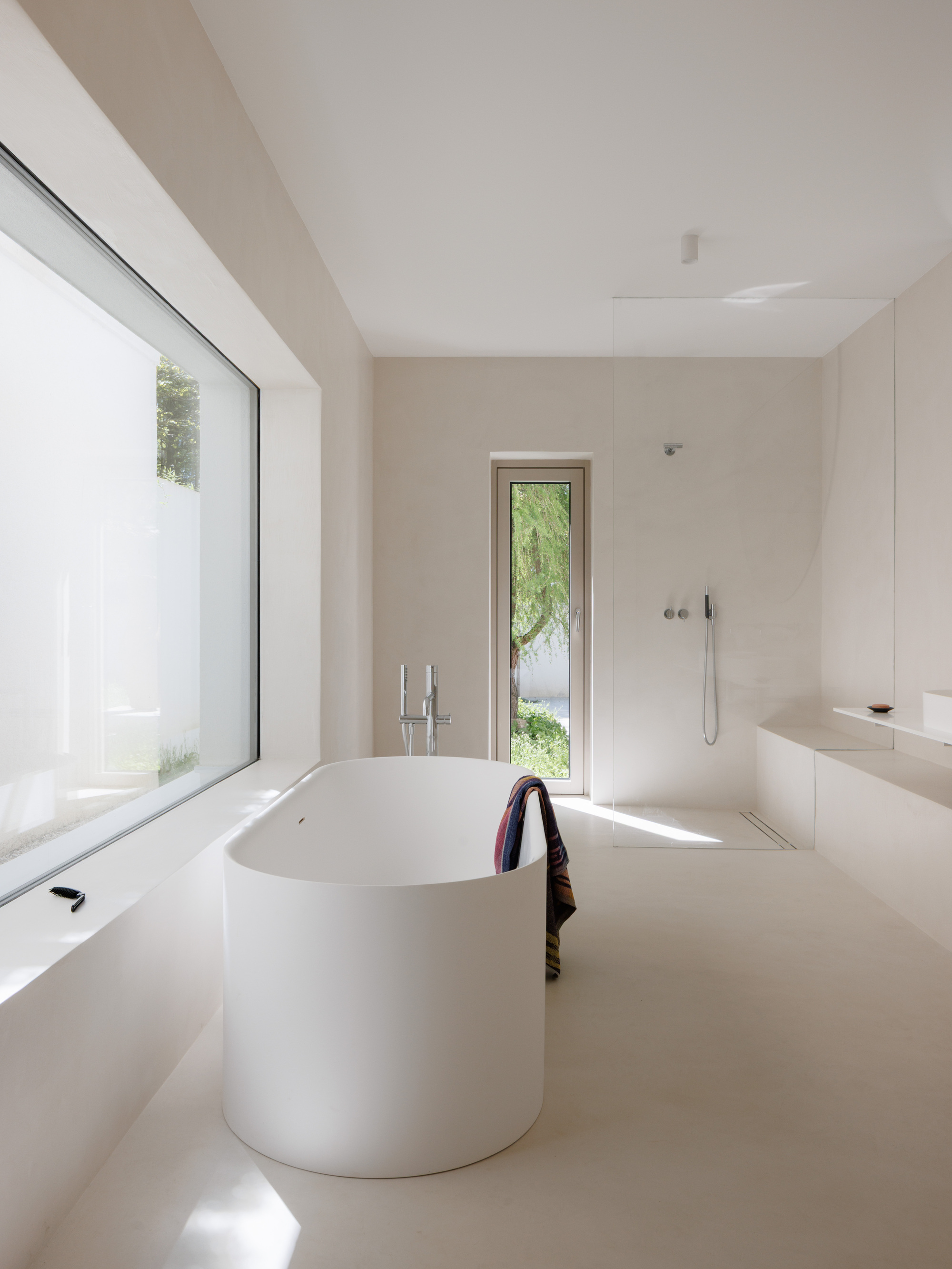 Freestanding cylindrical bathtub between a corner window and a narrow glazed door to the exterior