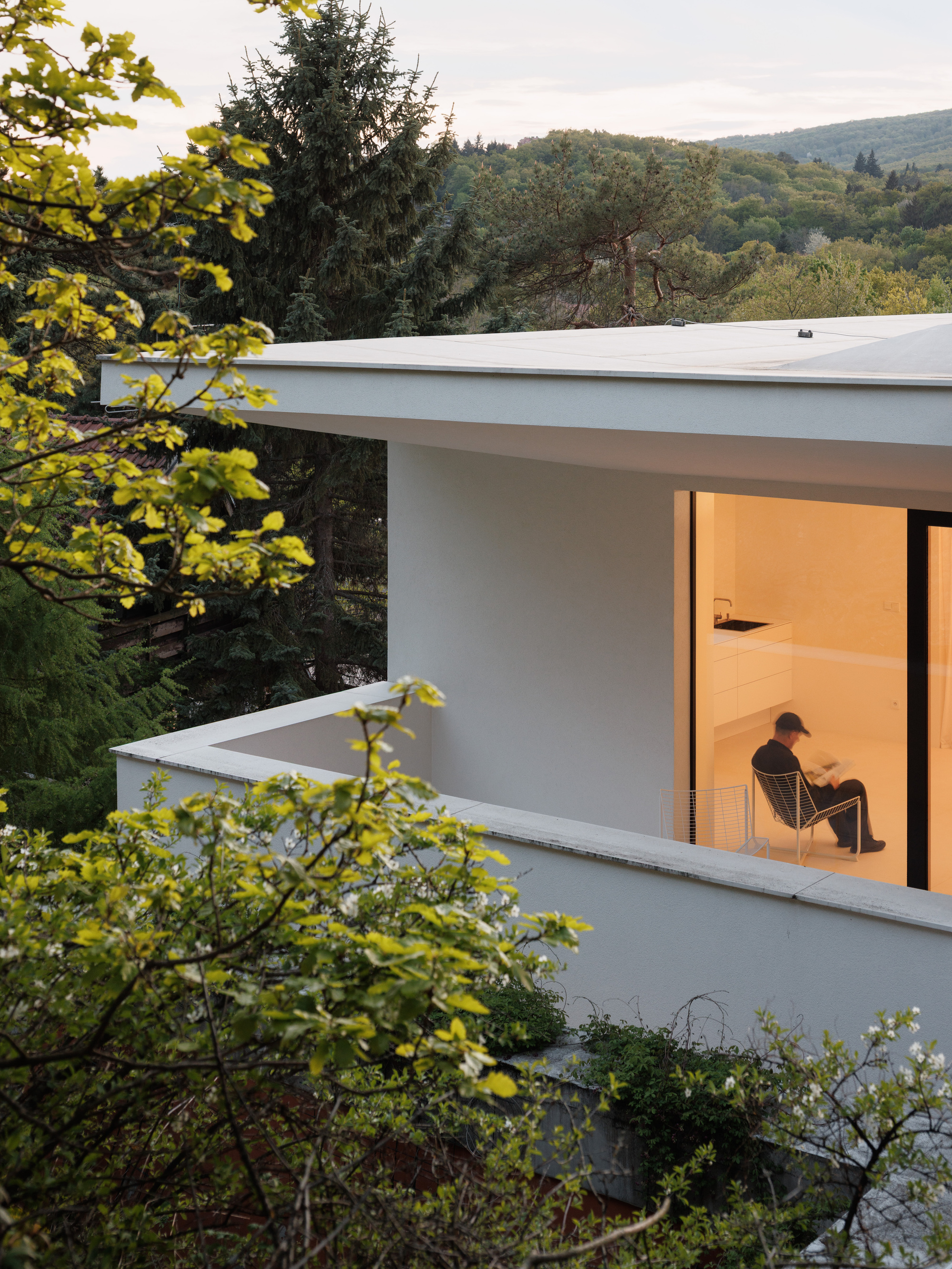 Corner terrace with flat white canopy and glazed opening where a person sits at dusk
