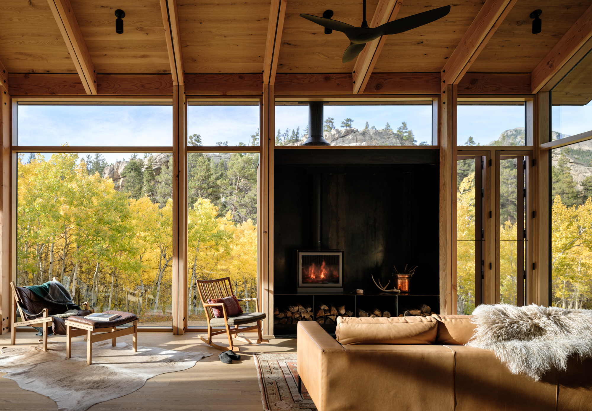Living room with black steel fireplace surround framed by full-height windows overlooking yellow-leaved aspens