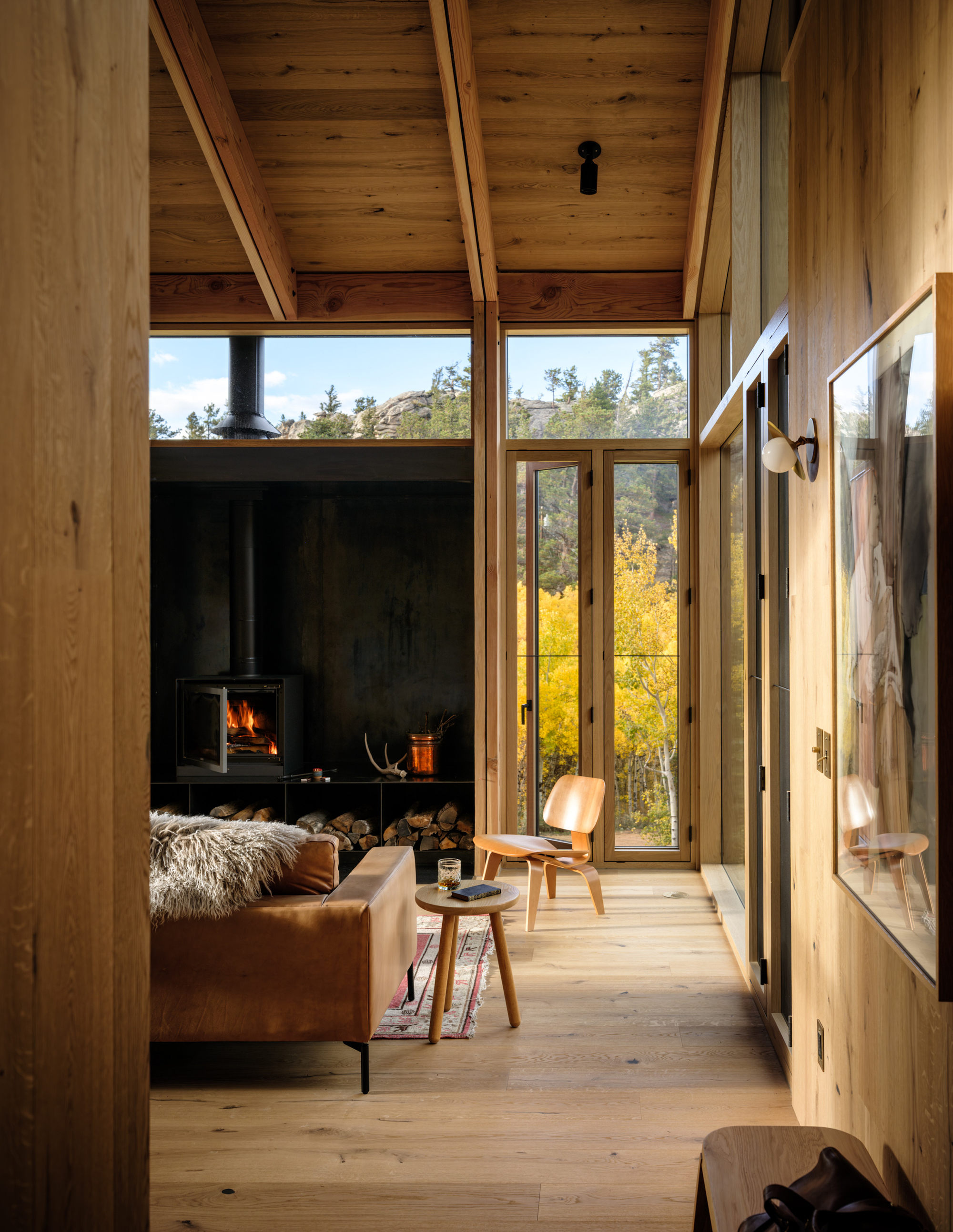 Wood-lined interior corridor with black steel fireplace surround and view to golden foliage