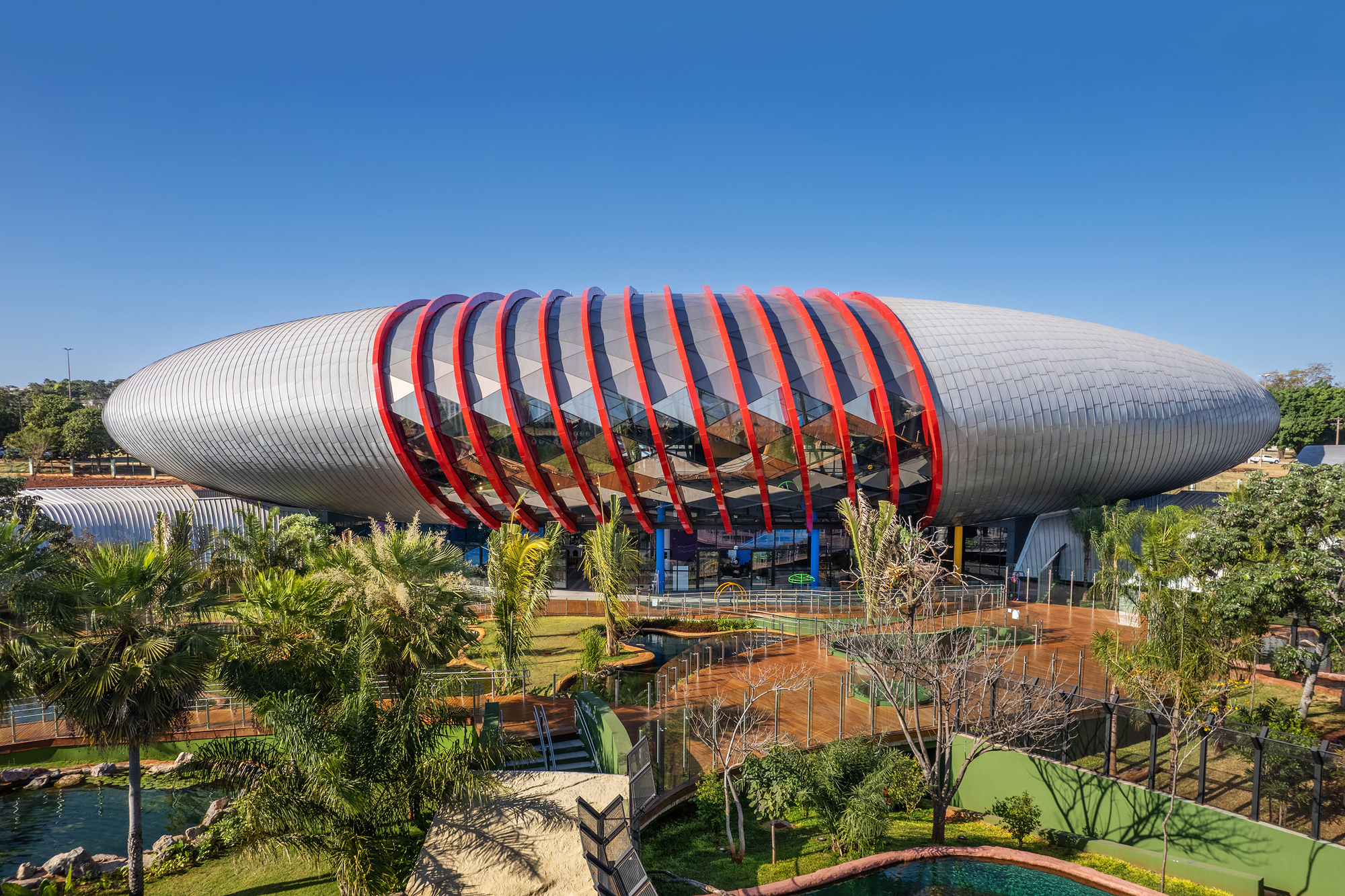 Elevated view of the elliptical ribbed metal roof with red structural bands above landscaped grounds