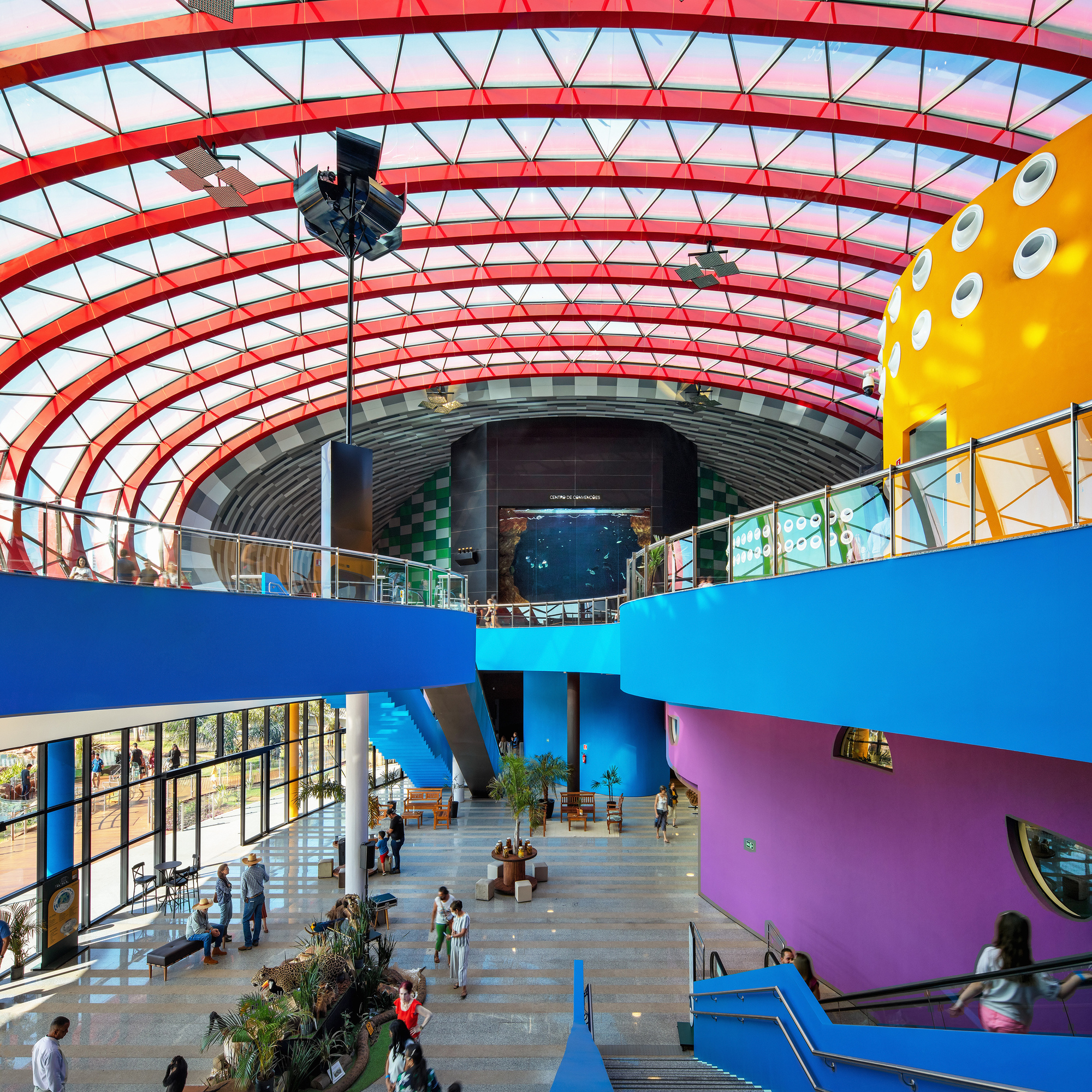 Interior atrium with curved blue and purple balconies beneath a glazed red steel rib structure