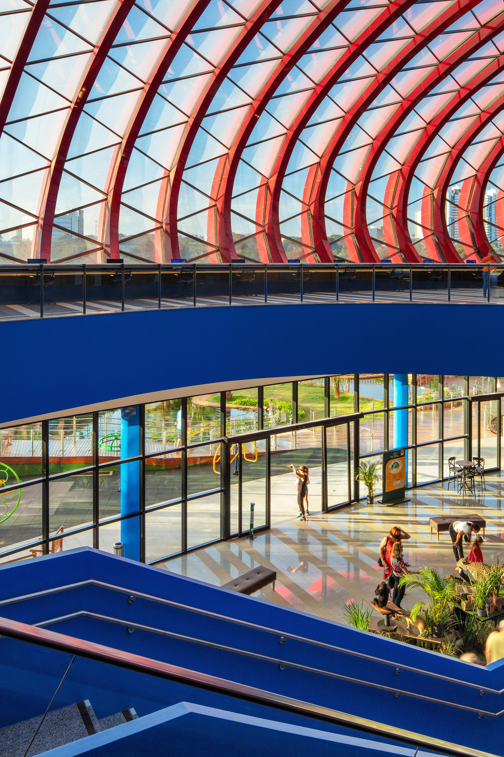 View down into the lobby showing red arched trusses over blue balcony levels and visitors below
