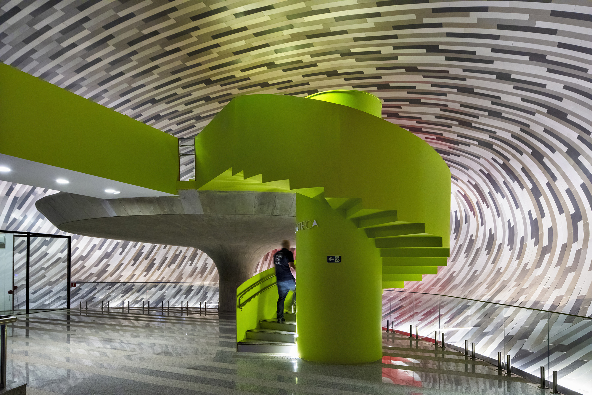 Lime green sculptural stair and foyer beneath a concentric ribbed ceiling with a visitor ascending