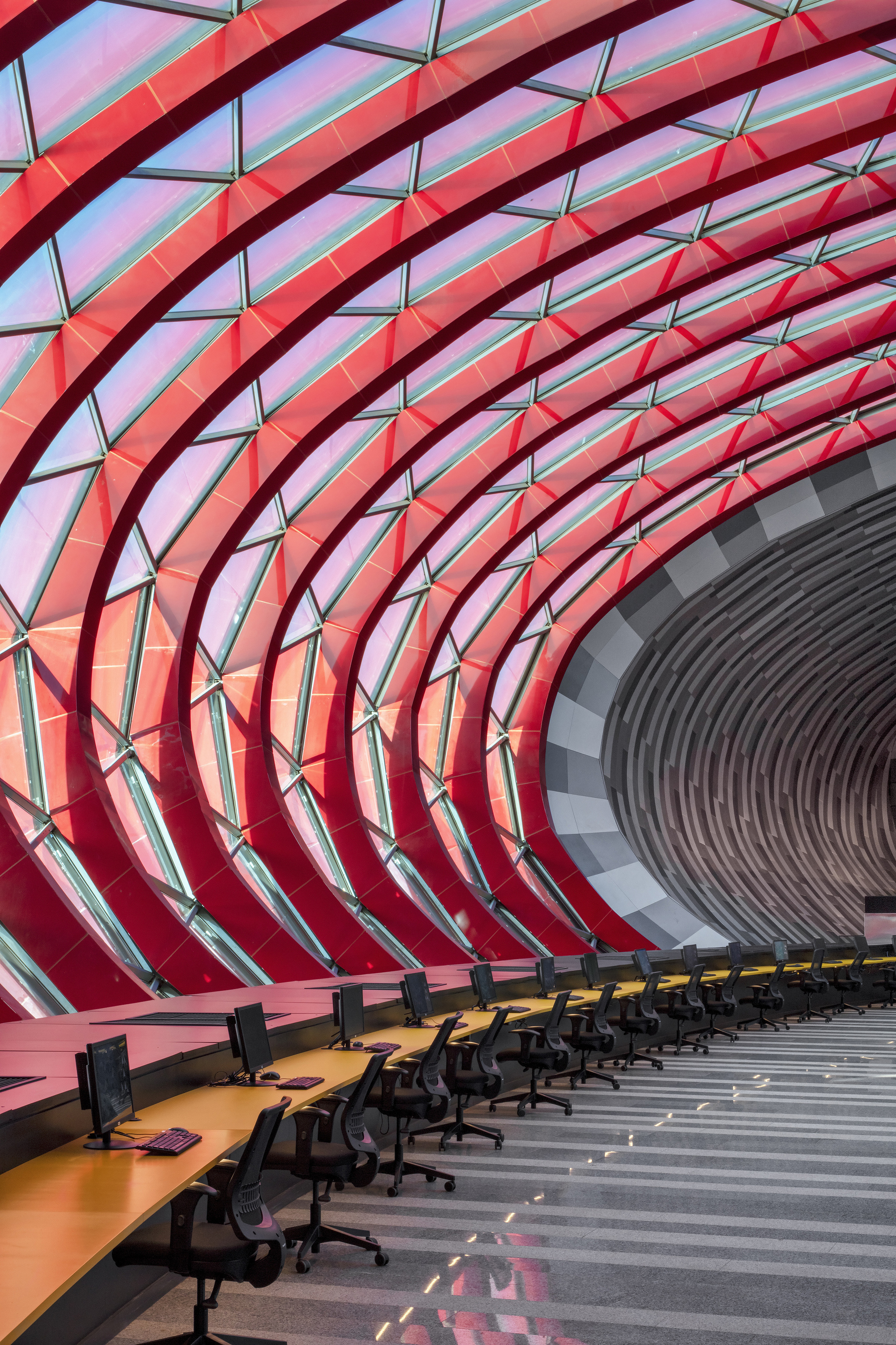 Interior workspace with curved red structural ribs and glazing panels wrapping overhead in a tunnel form
